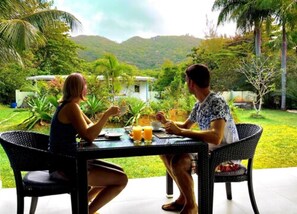 Two people dining at an outdoor table with a view of a lush garden and hills in the background.