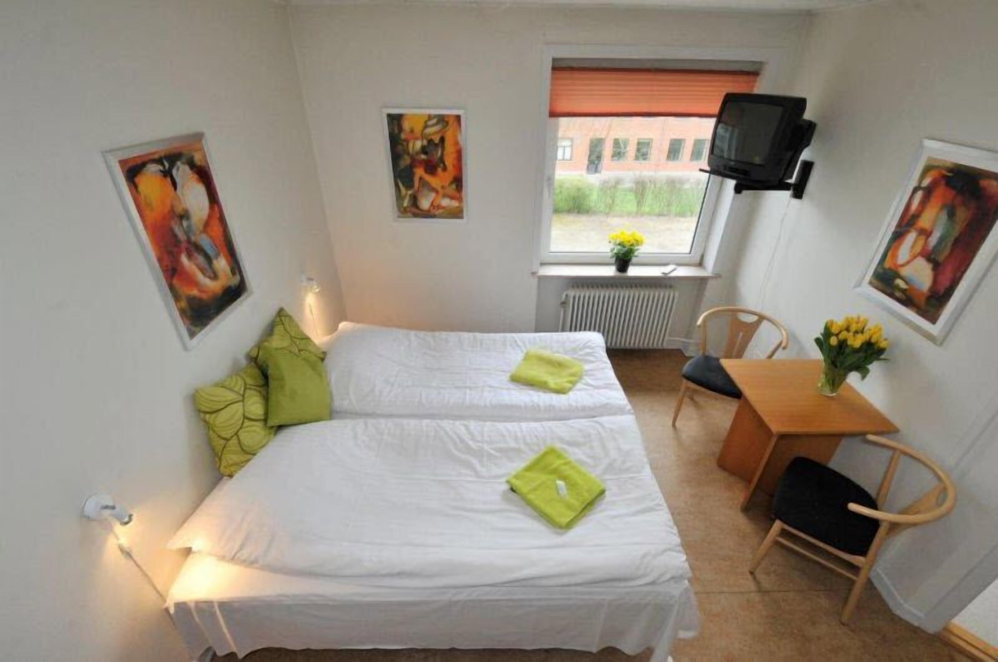 Et lille, rent værelse med to senge, et lille bord med stol, et TV ophængt på væggen og et vindue med udsigt.