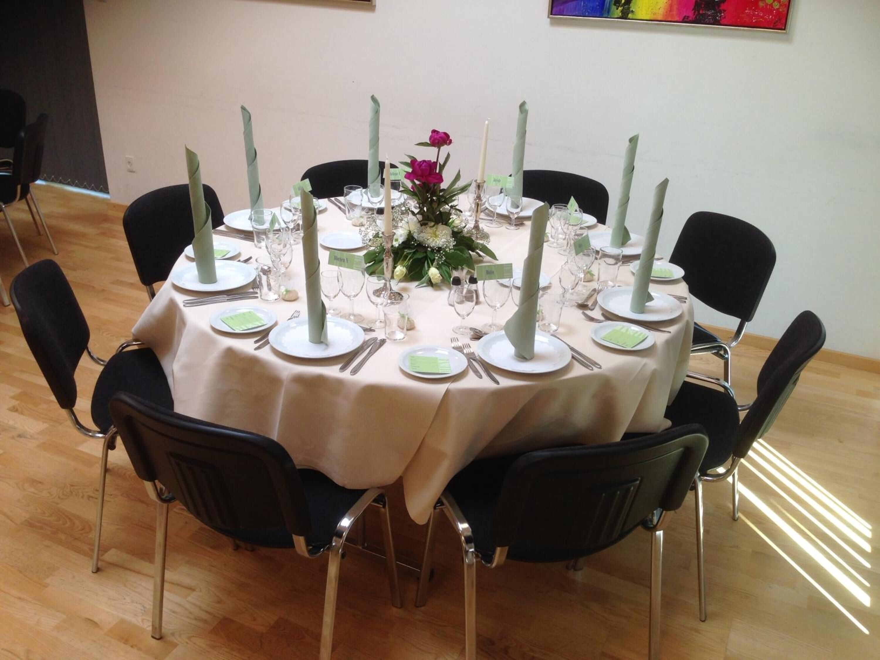 A round table set for a formal event with white tablecloths, green napkins, and tall candles.