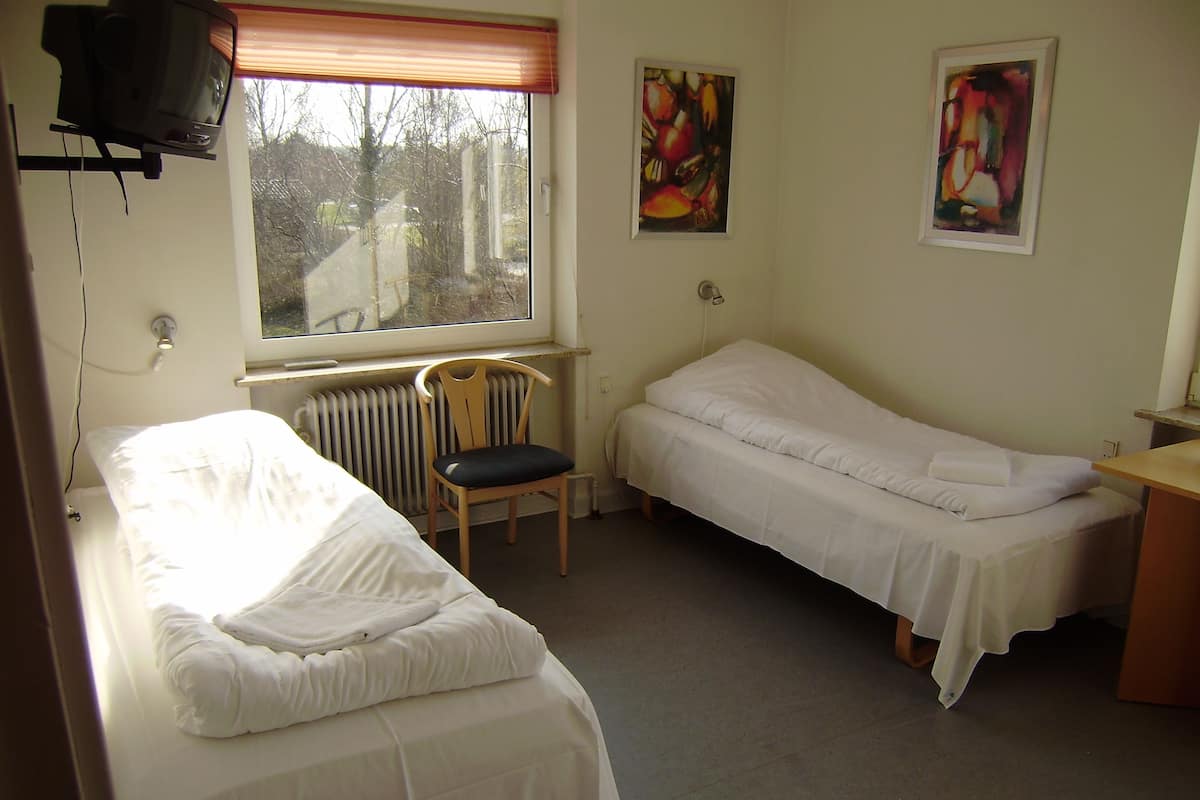 A small, clean room with two single beds, a chair, a radiator, and two abstract paintings on the wall.