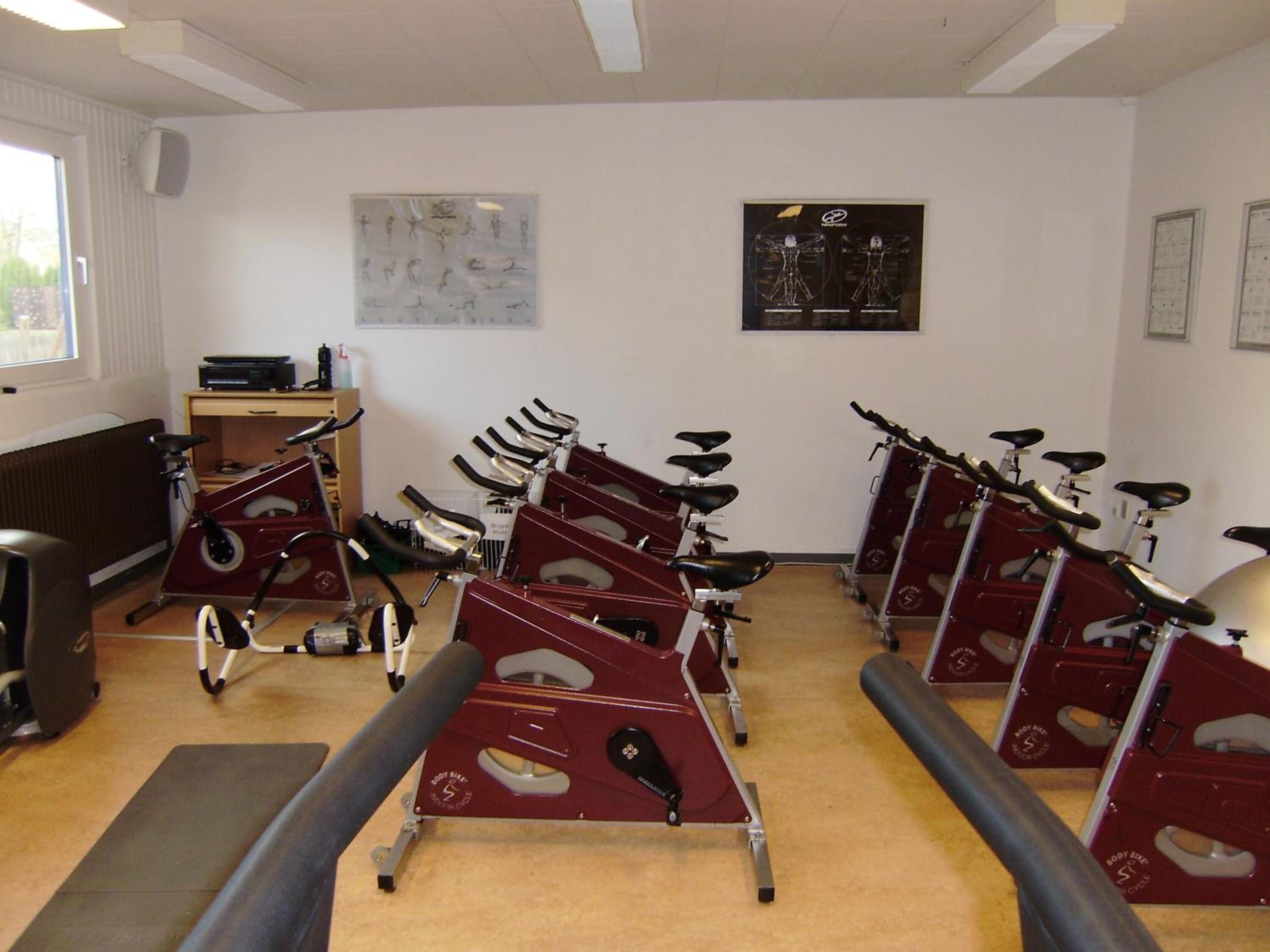 A gym with stationary bikes arranged in rows, a radiator, a small desk with a chair, and a window.
