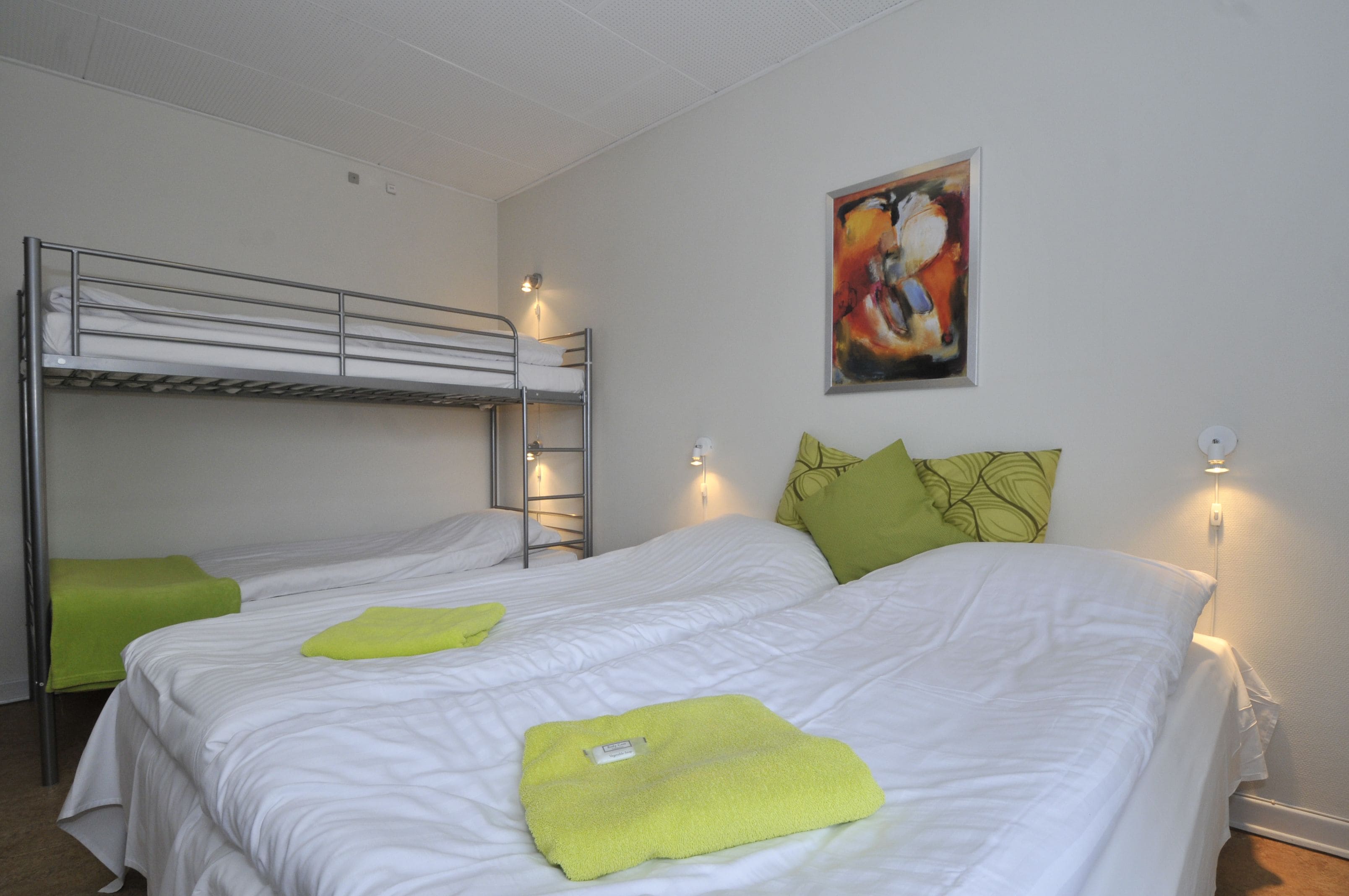 A hotel room with bunk beds, a painting on the wall, and a green pillow on one bed.
