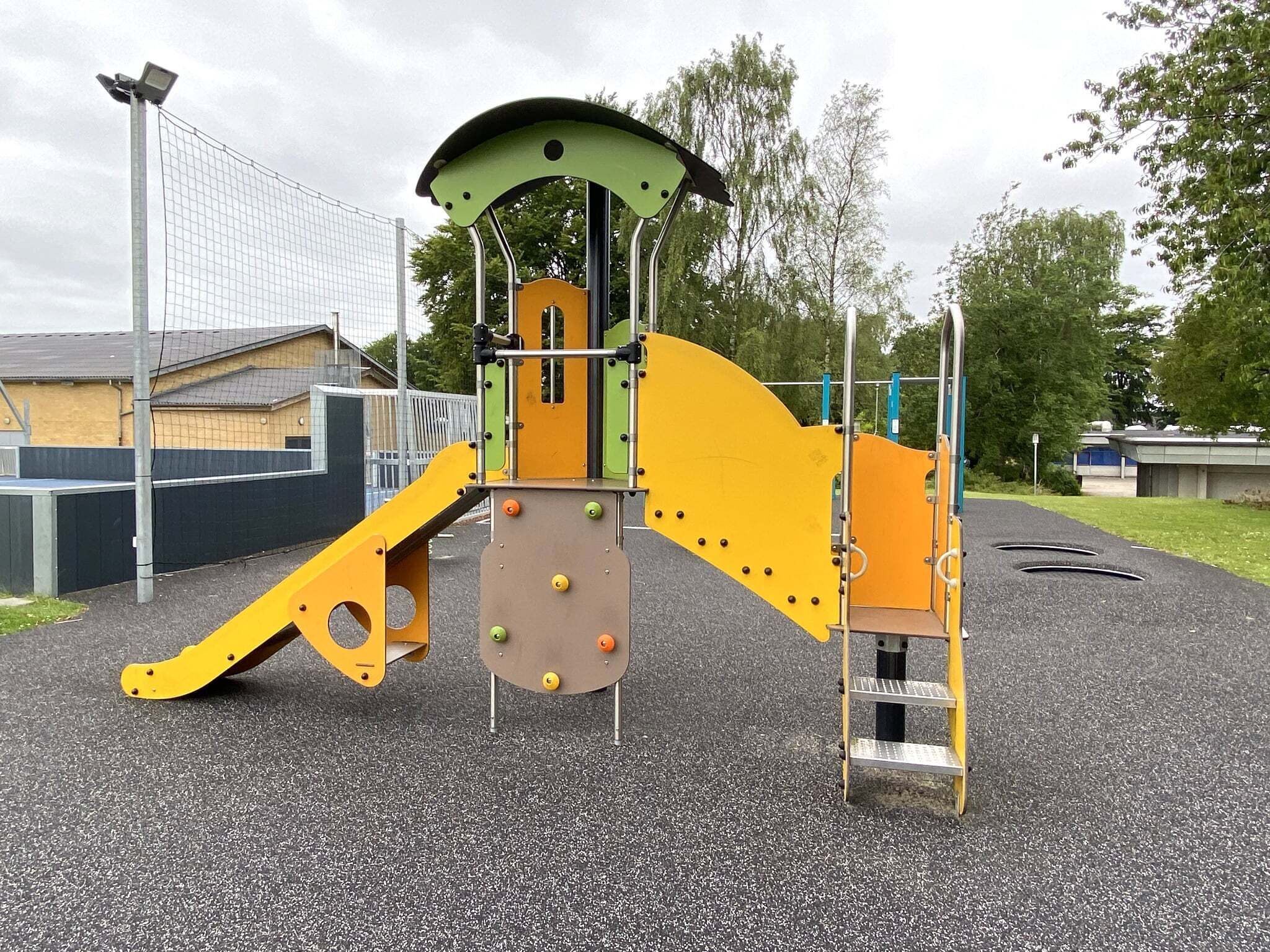 A playground with a climbing structure, a slide, and a ladder.