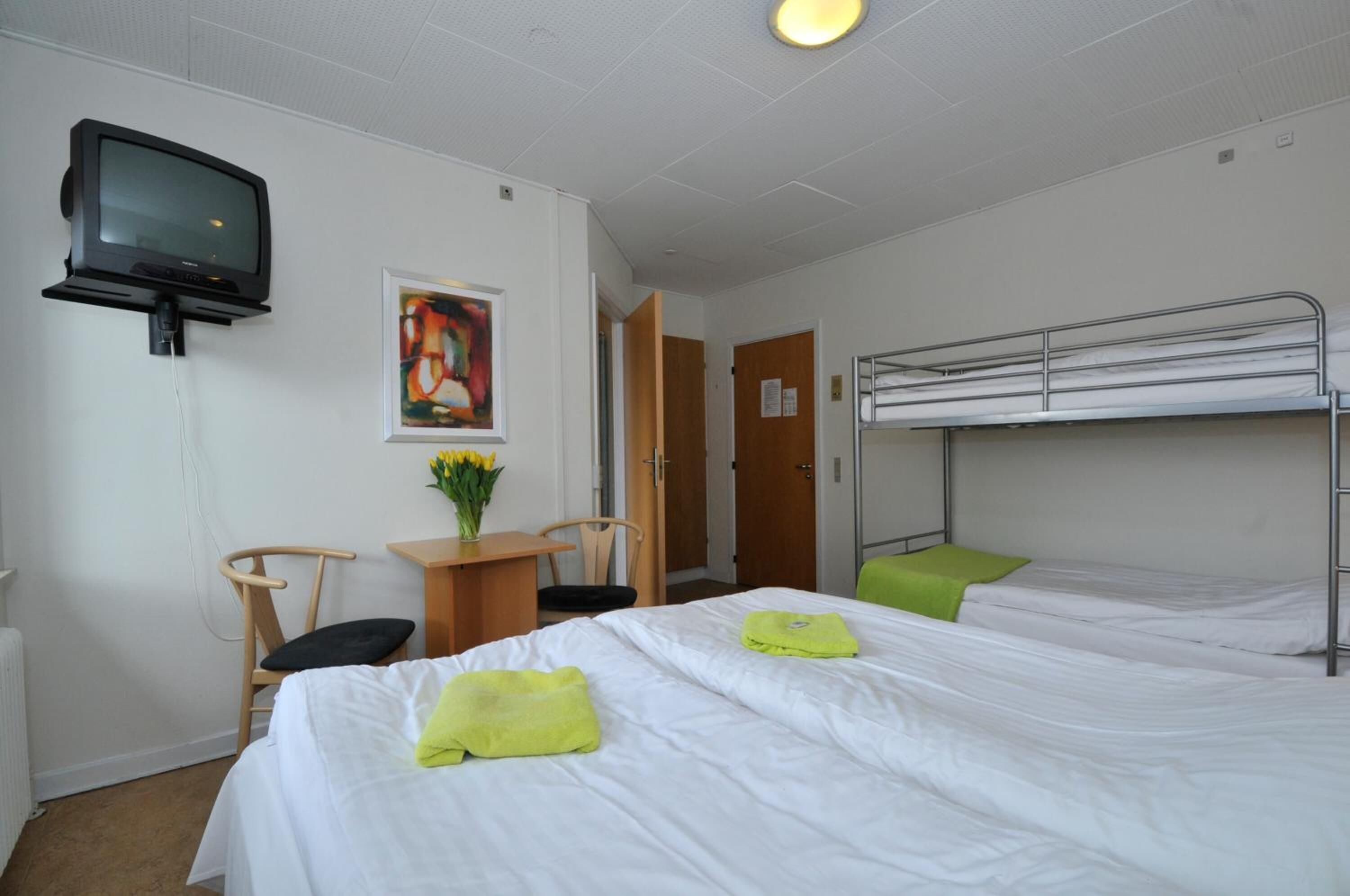 Une chambre d’hôtel avec deux lits, un bureau avec une chaise, une télévision et un tableau au mur.