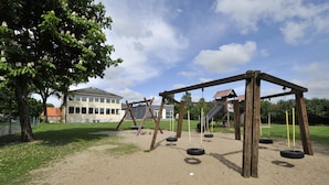 Un parque infantil con columpios y un árbol, y un edificio al fondo.