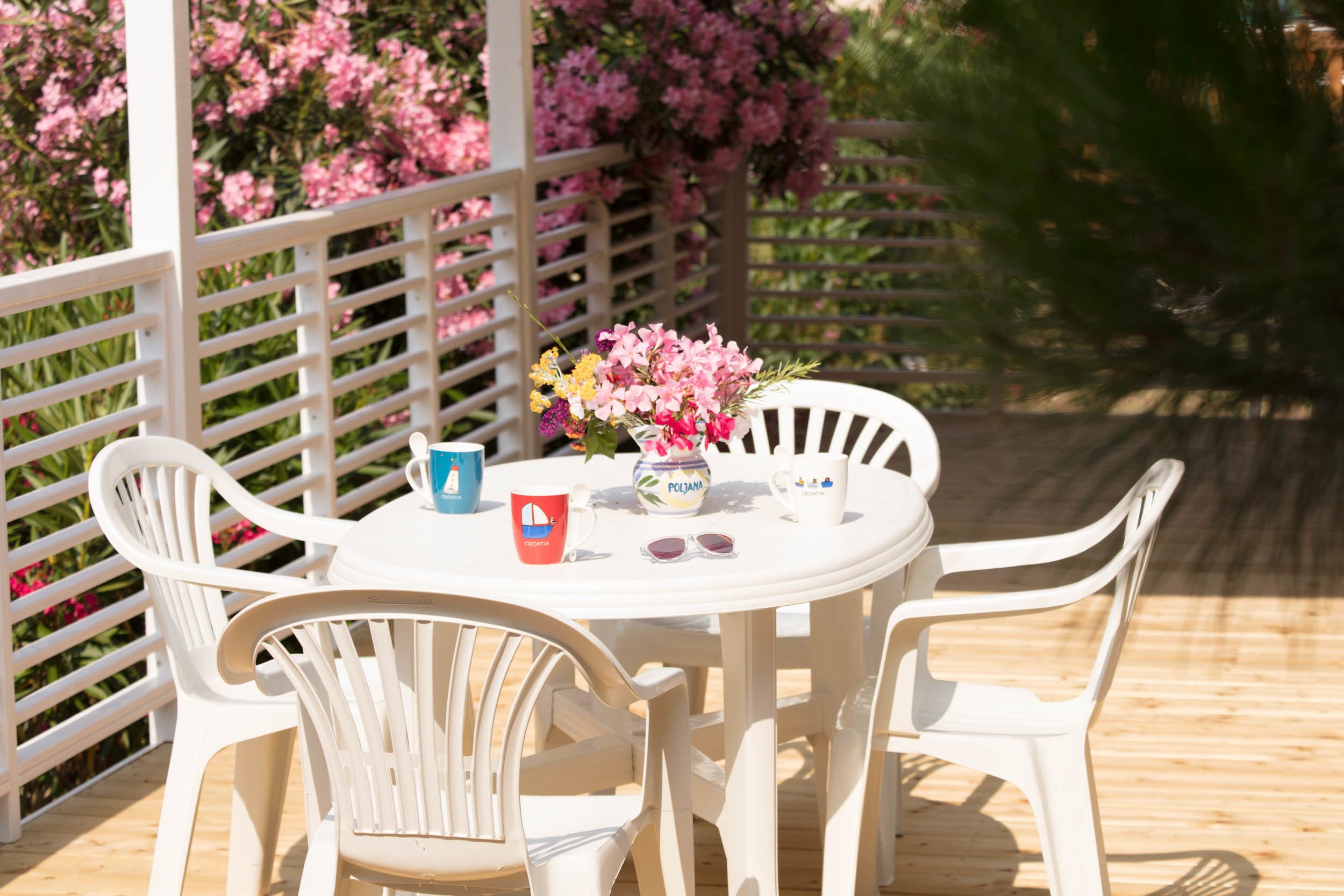 A white outdoor table with chairs, a vase with flowers, and a mug.