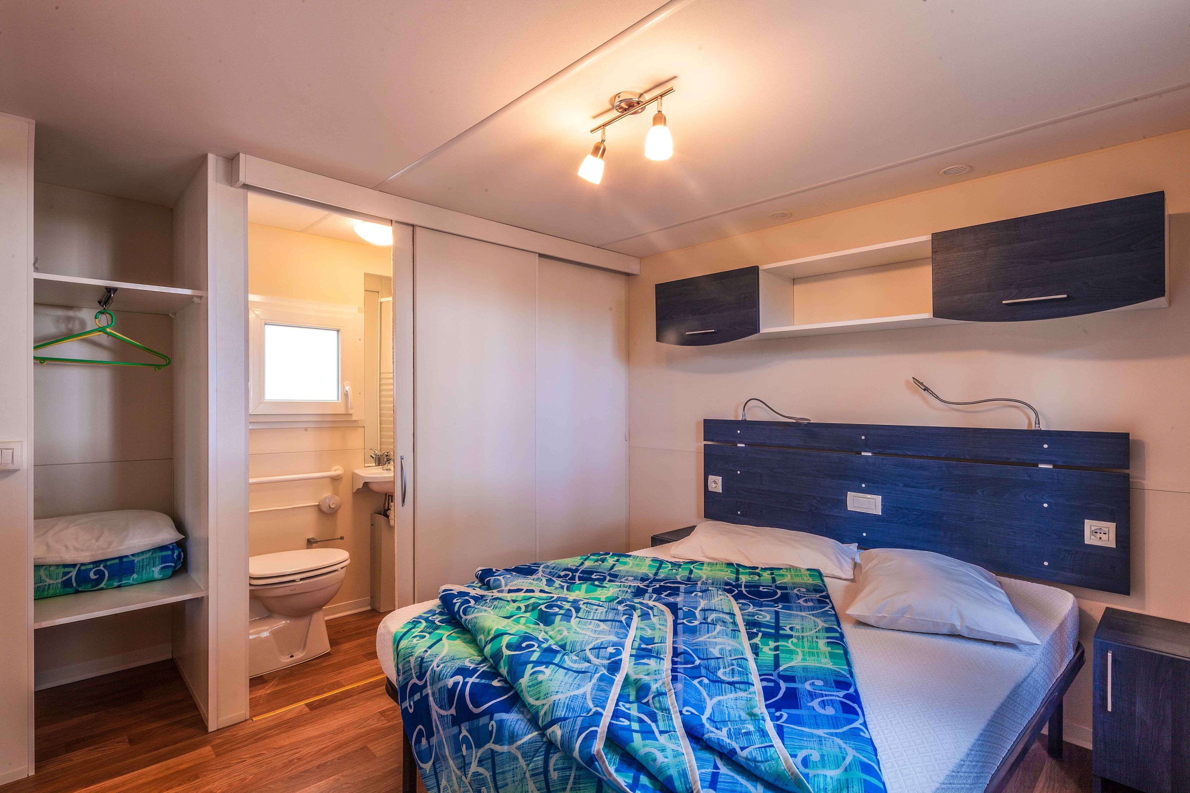 Ein Schlafzimmer mit Bett, Nachttisch, Kleiderschrank und einem Badezimmer mit Toilette und Waschbecken.