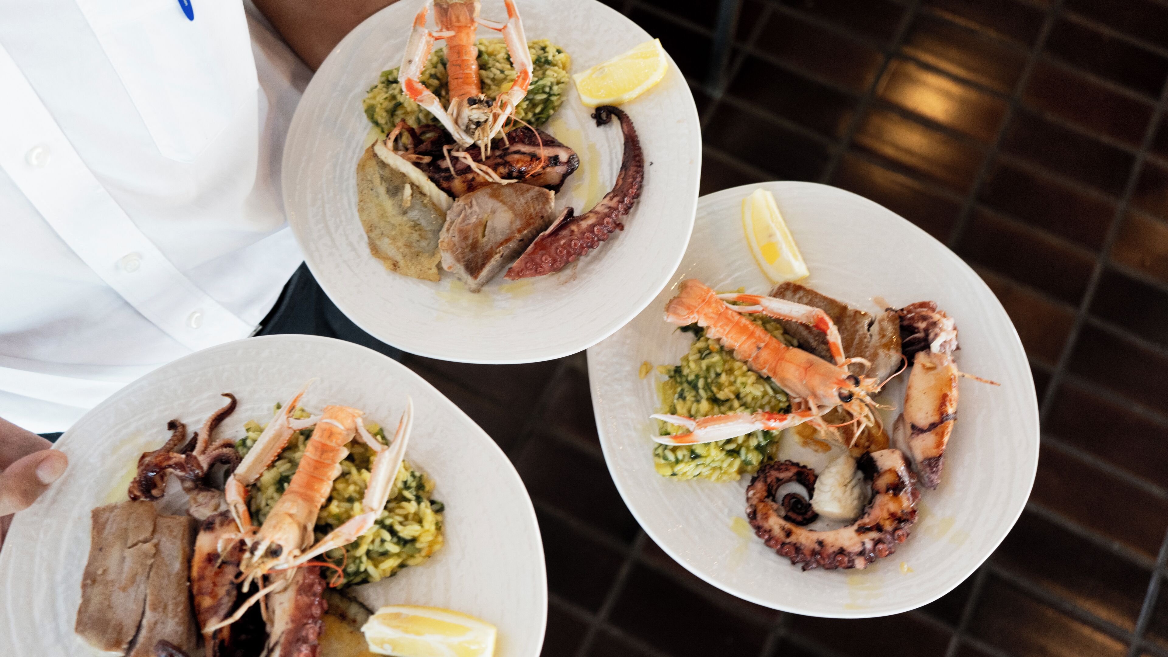Three plates of seafood with lemon wedges, held by a person in a white shirt.