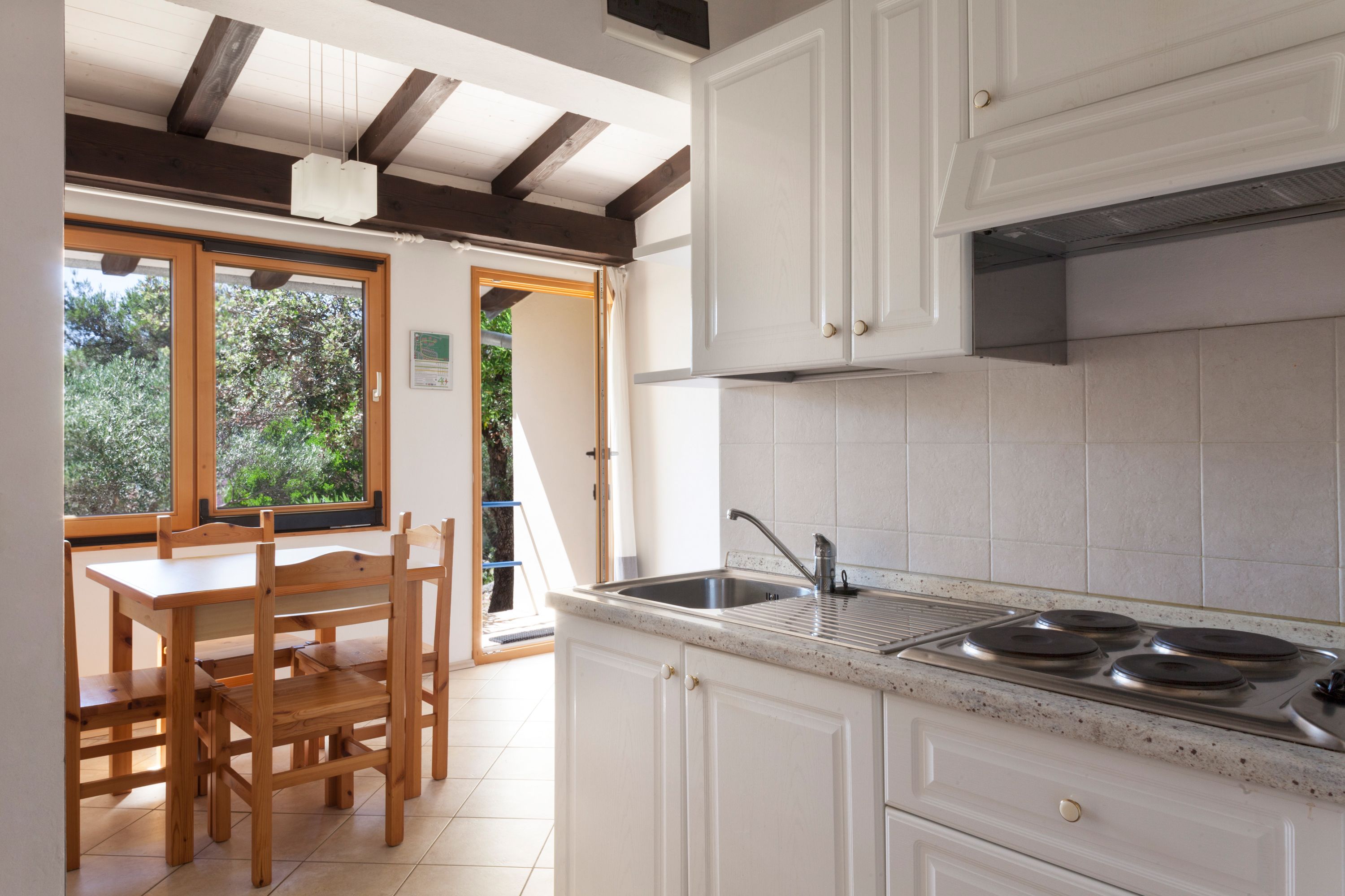 A kitchen with white cabinets, a stainless steel sink, and a wooden dining table with chairs.