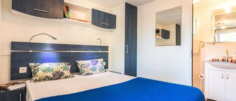 A modern bedroom with a large bed, a nightstand, a wardrobe, and a bathroom with a sink and mirror.