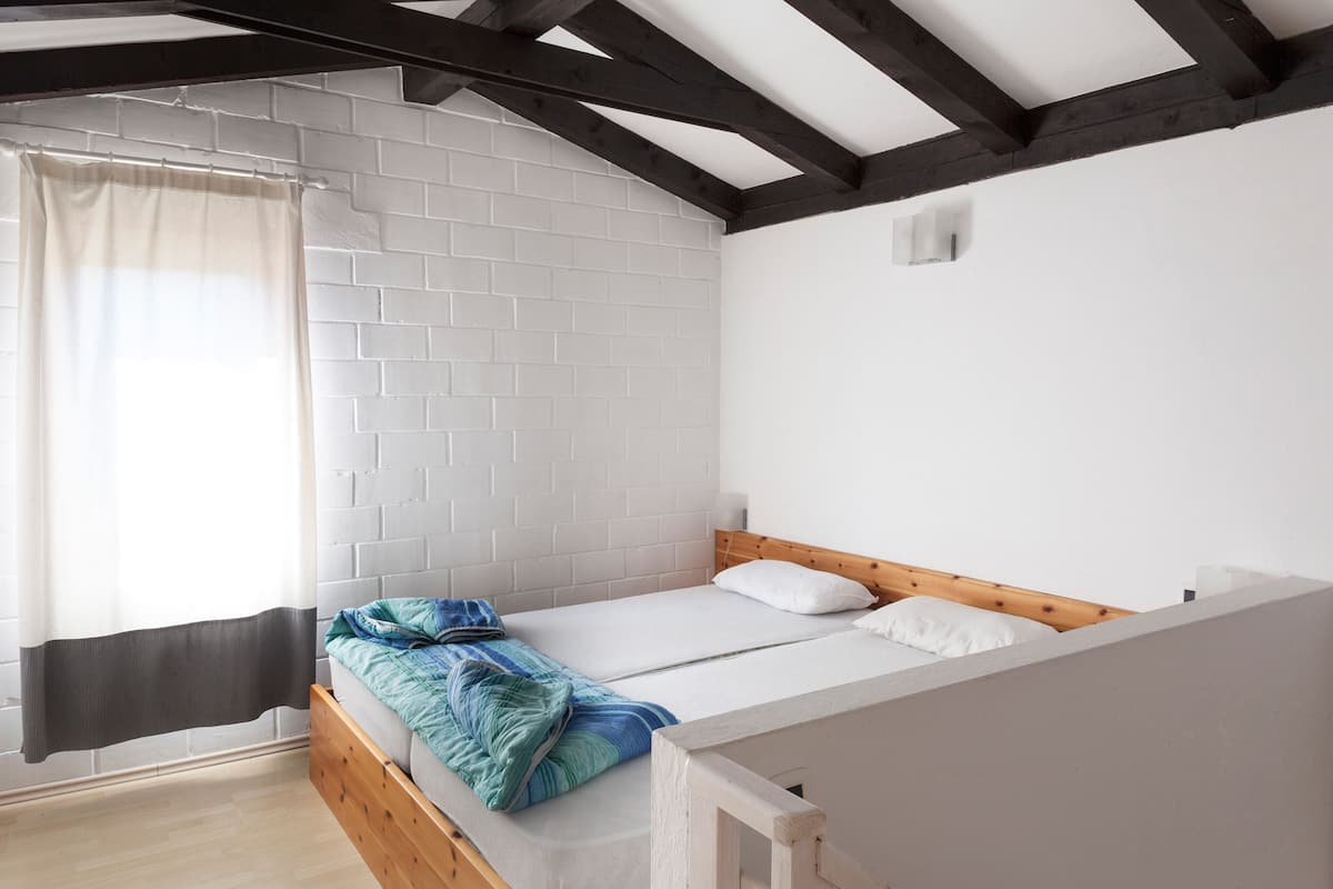 Een eenpersoonsbed met houten hoofdeinde in een kamer met witte bakstenen muren en zichtbare houten balken.