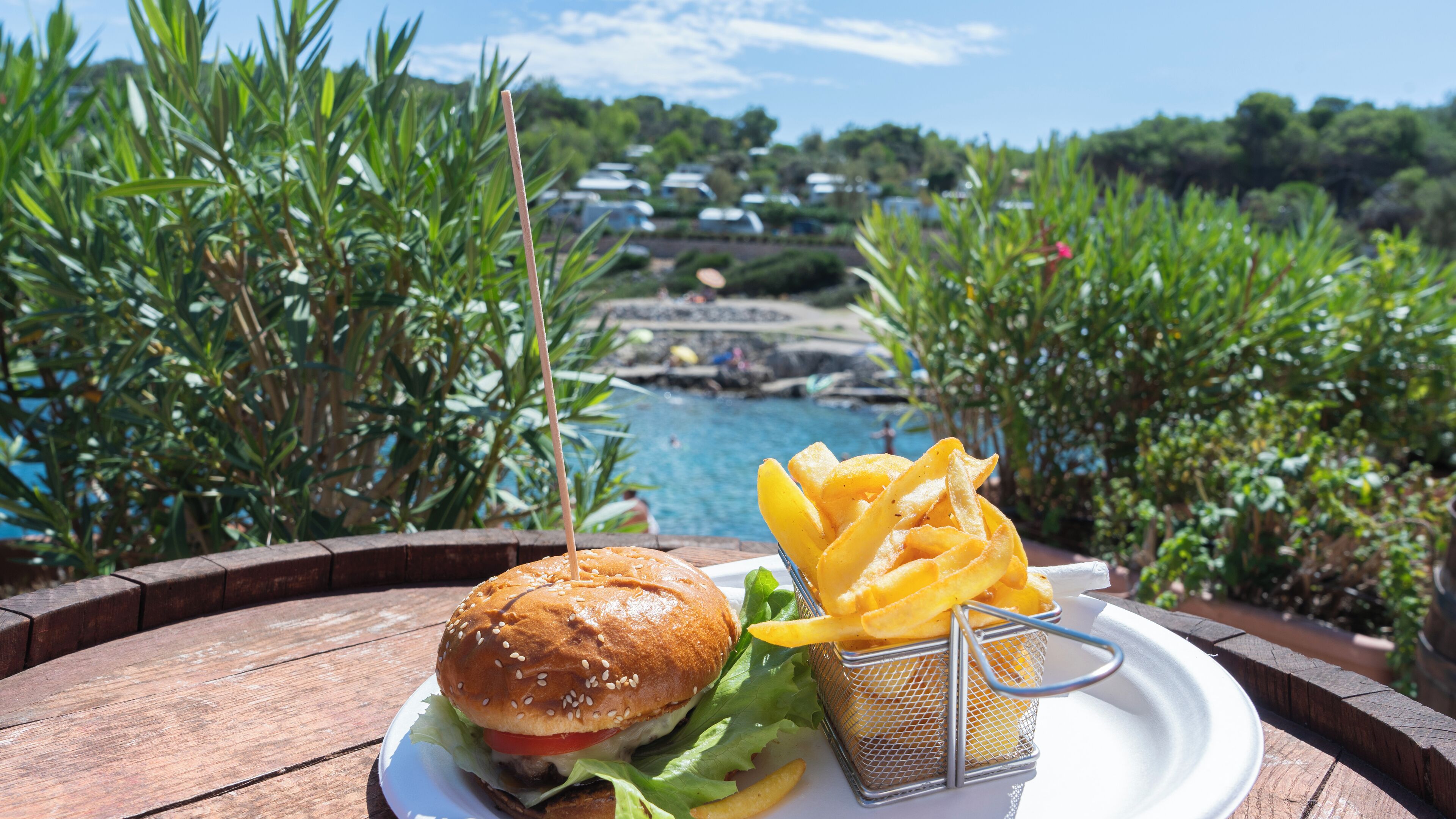 A meal of a burger and fries on a wooden table with a view of a pool and greenery.