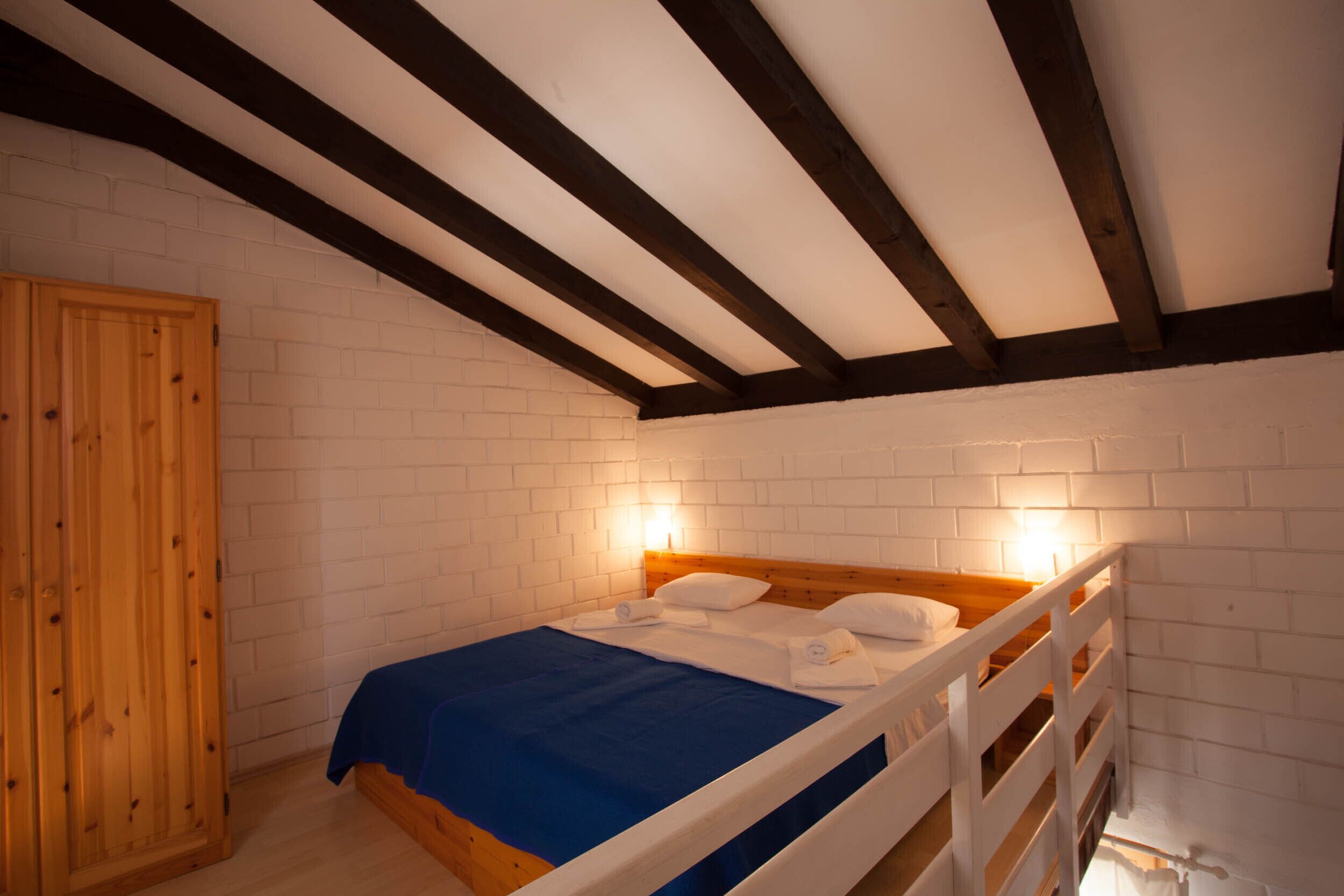 A bedroom with a wooden bed, white brick walls, and exposed wooden beams on the ceiling.