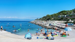 Ein Strand mit klarem, blauem Wasser, felsigem Ufer und Menschen bei verschiedenen Aktivitäten.