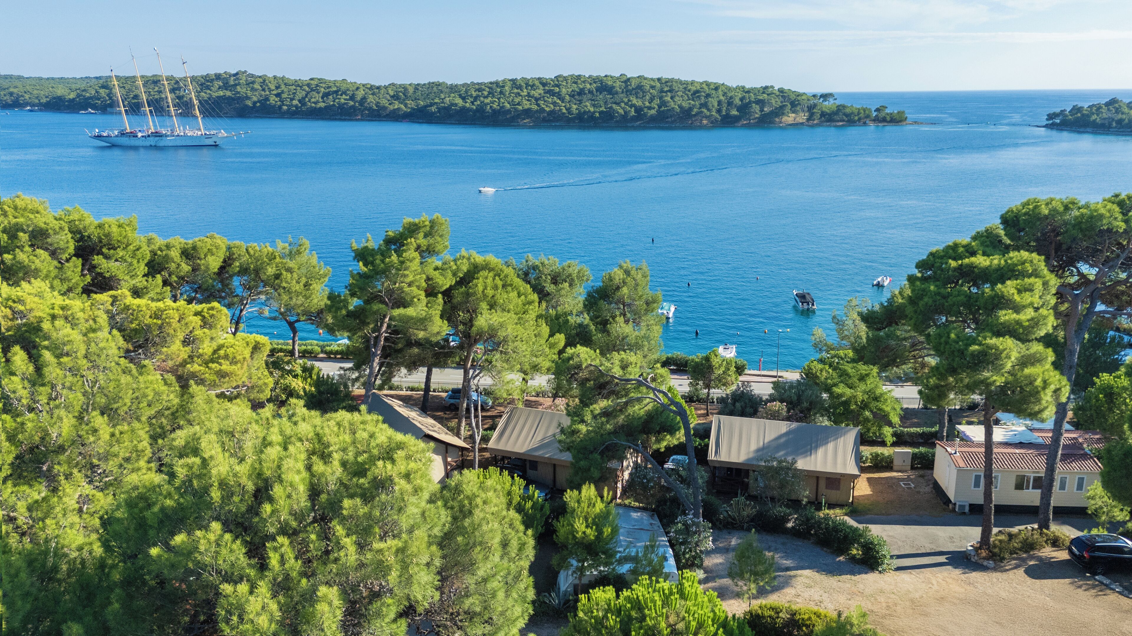 A coastal property with a view of the sea, a sailboat, and a forested area.