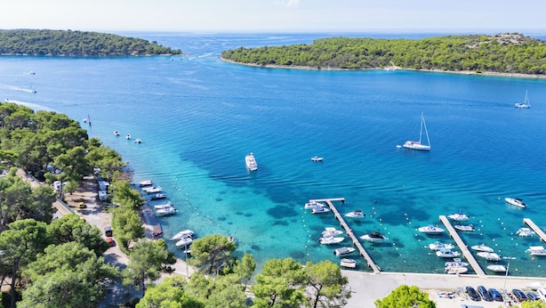 Ein Yachthafen mit vertäuten Booten, umgeben von üppigen grünen Hügeln und klarem, blauem Wasser.