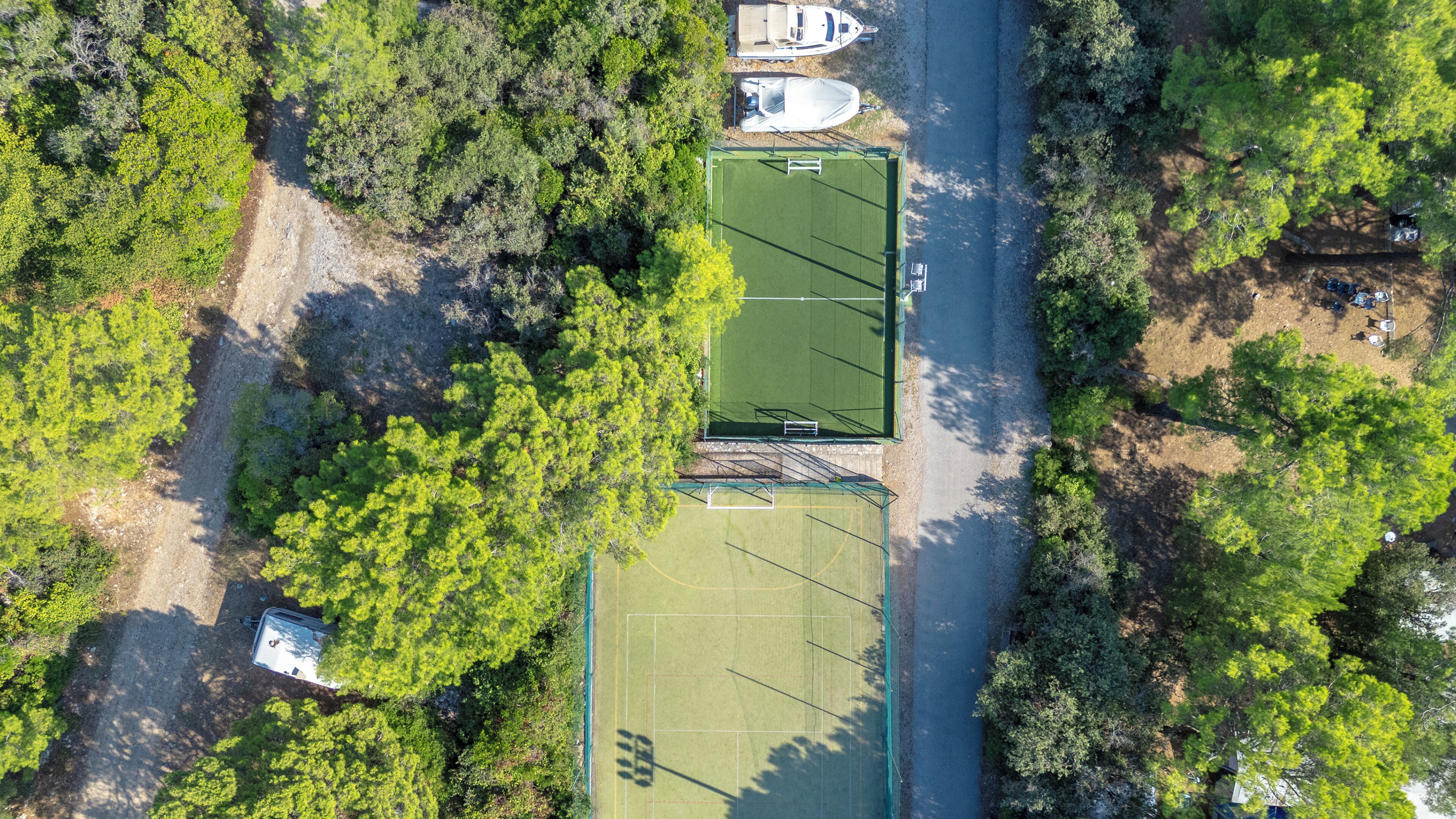Vista aérea de una propiedad con cancha de tenis, zona de estacionamiento y vegetación circundante.