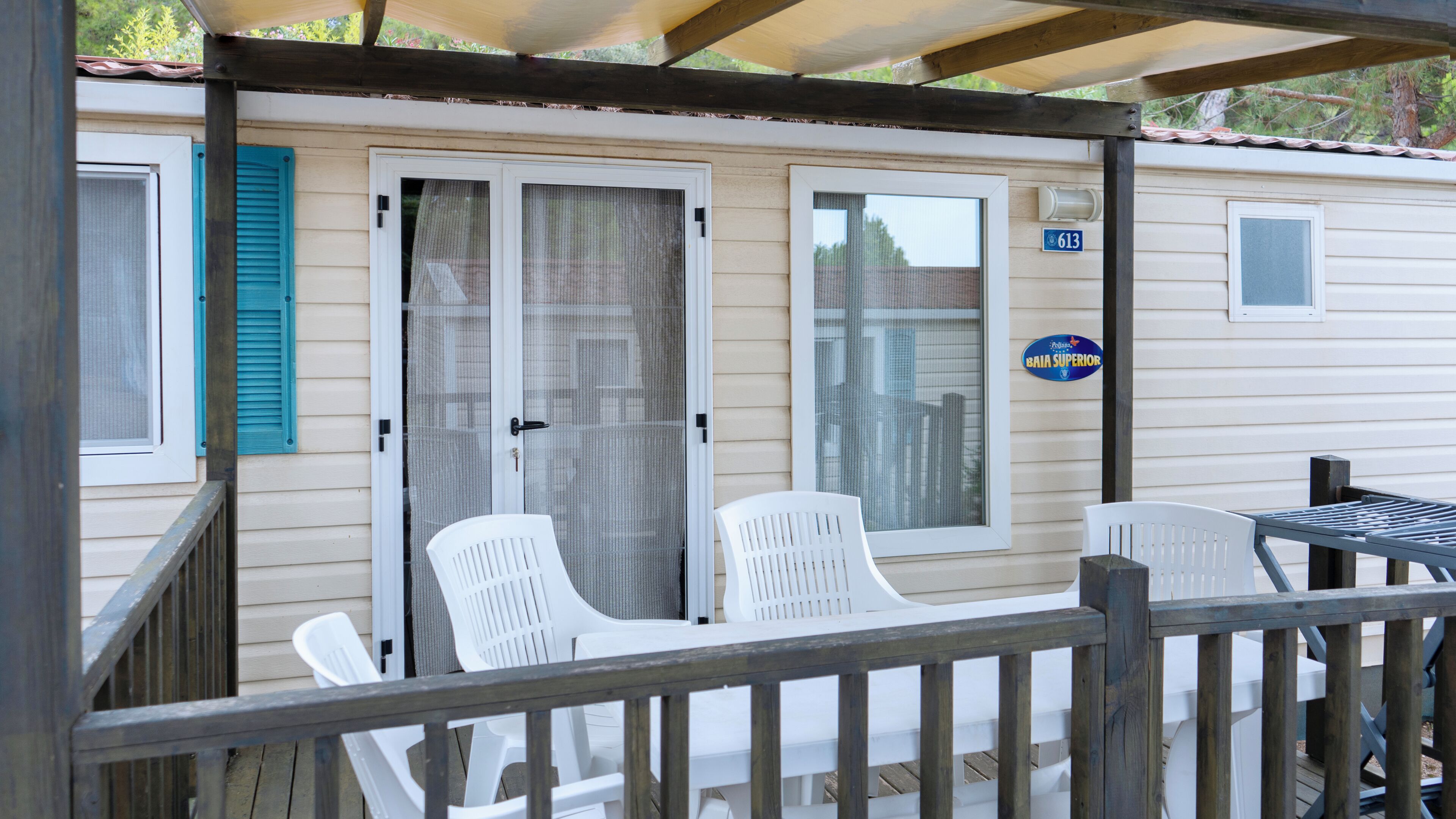 A mobile home with a covered porch, two white plastic chairs, and a small table.