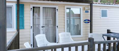 Une maison mobile dotée d’un porche couvert, de deux chaises en plastique blanches et d’une petite table.