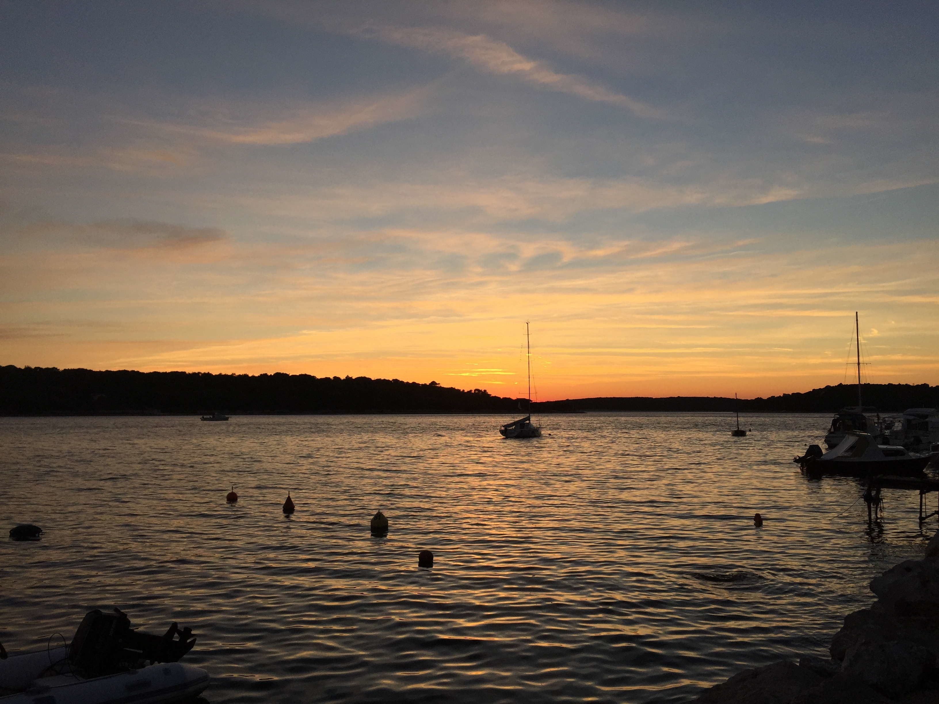 A sunset over a calm body of water with boats and a dock.