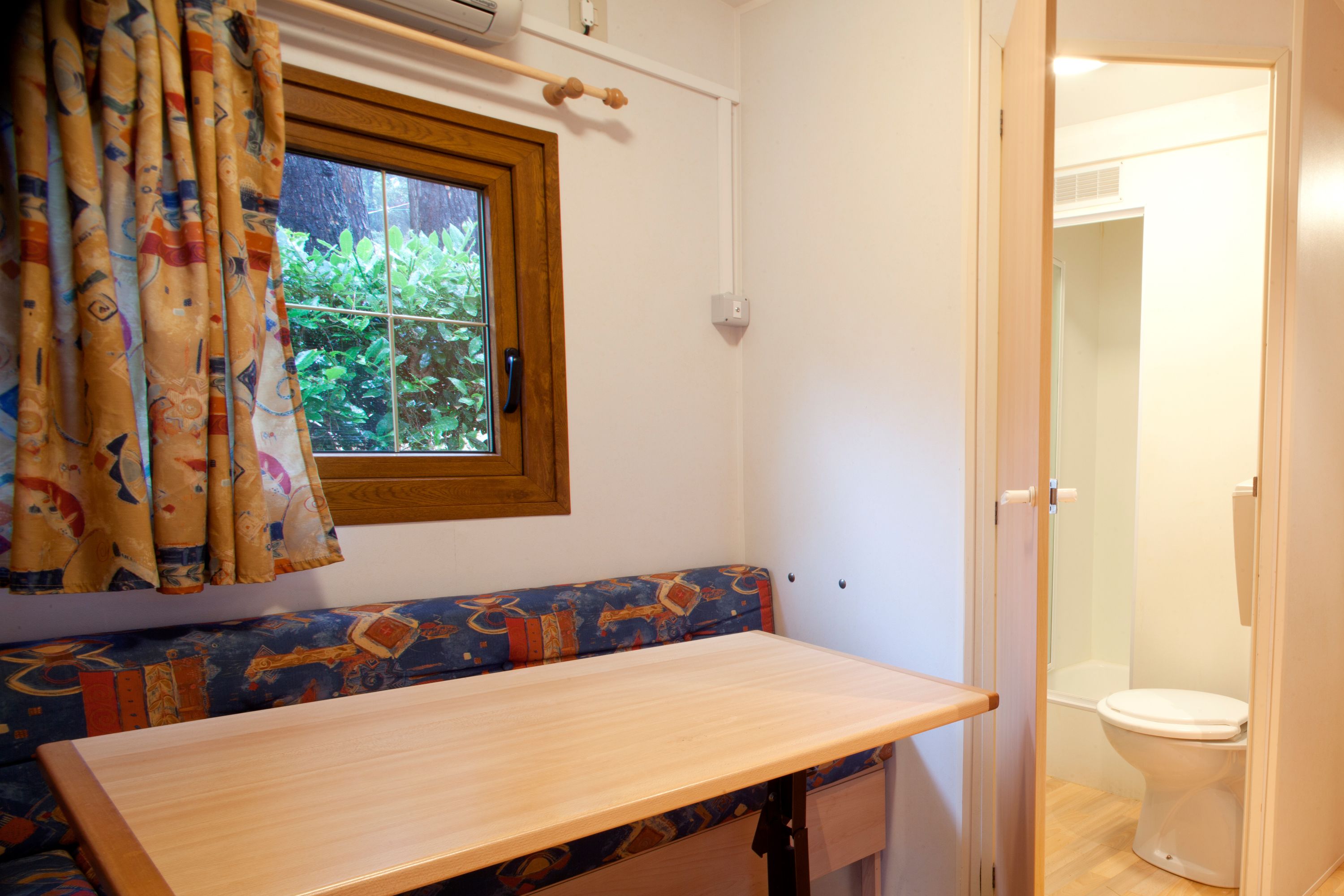 A bathroom with a wooden bench, a window with curtains, and a toilet.