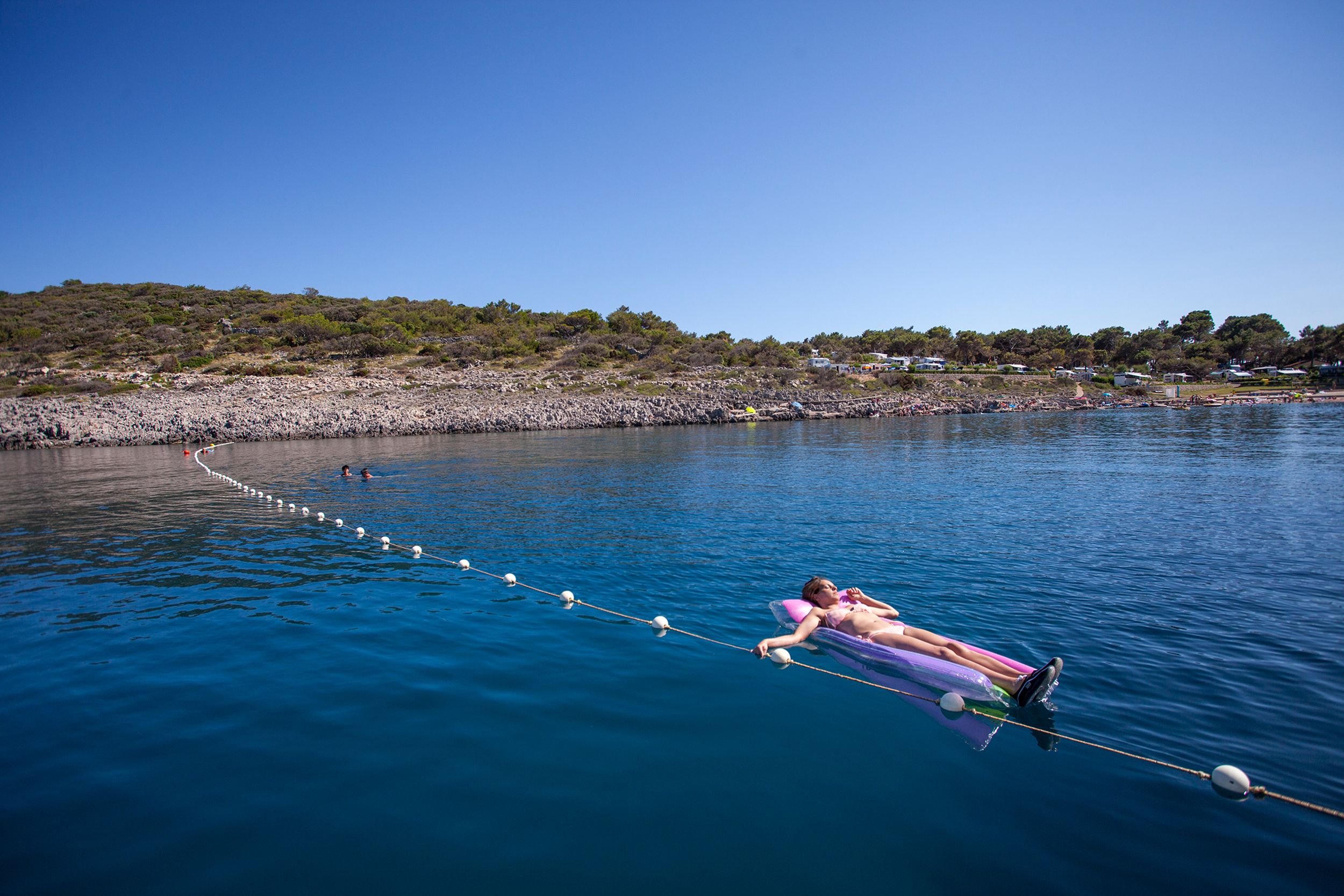 A person lying on a floating platform in a body of water, connected by a rope.