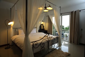 A four-poster bed with a canopy, a bedside table with a lamp, and a view of the outdoors through a sliding glass door.