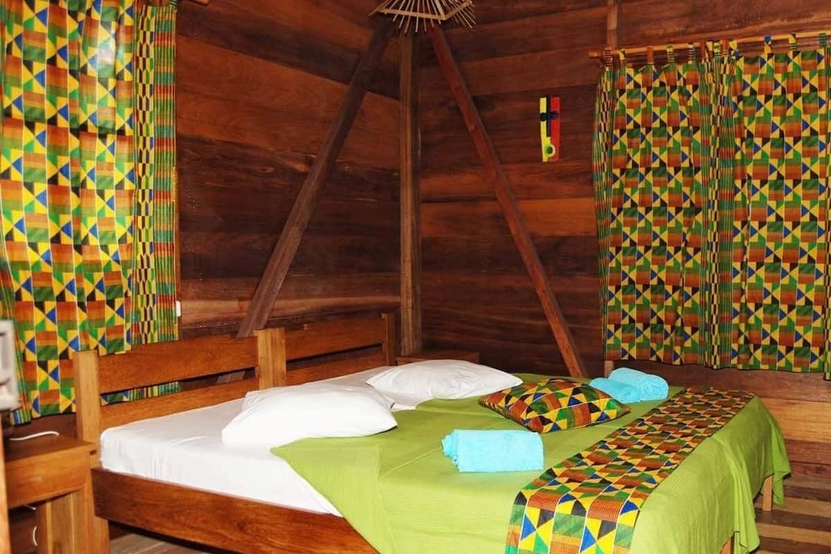 A wooden cabin room with a bed, a wooden dresser, and a window with curtains.