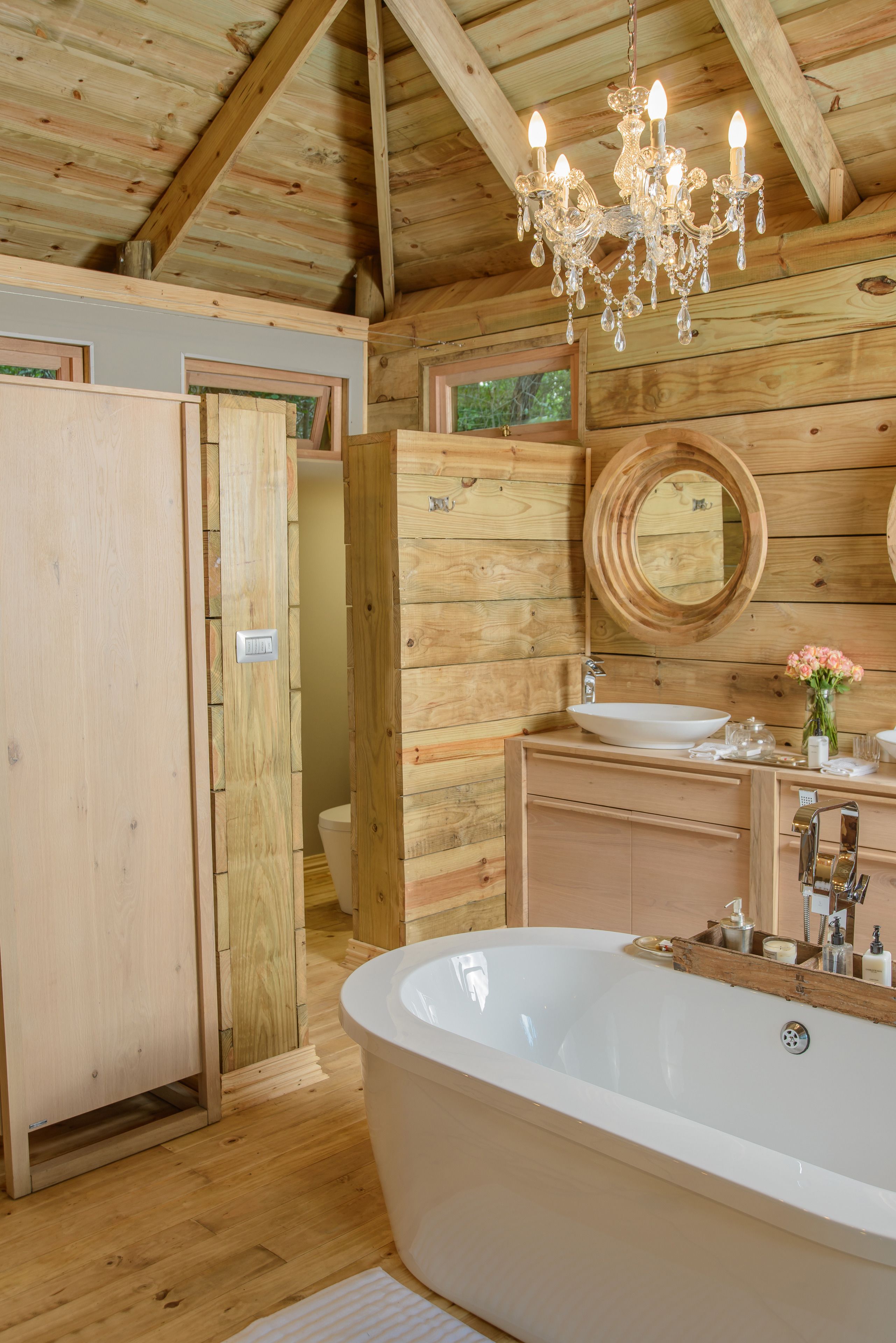 A wooden cabin bathroom with a freestanding bathtub, wooden cabinets, a vanity with a sink, and a chandelier.