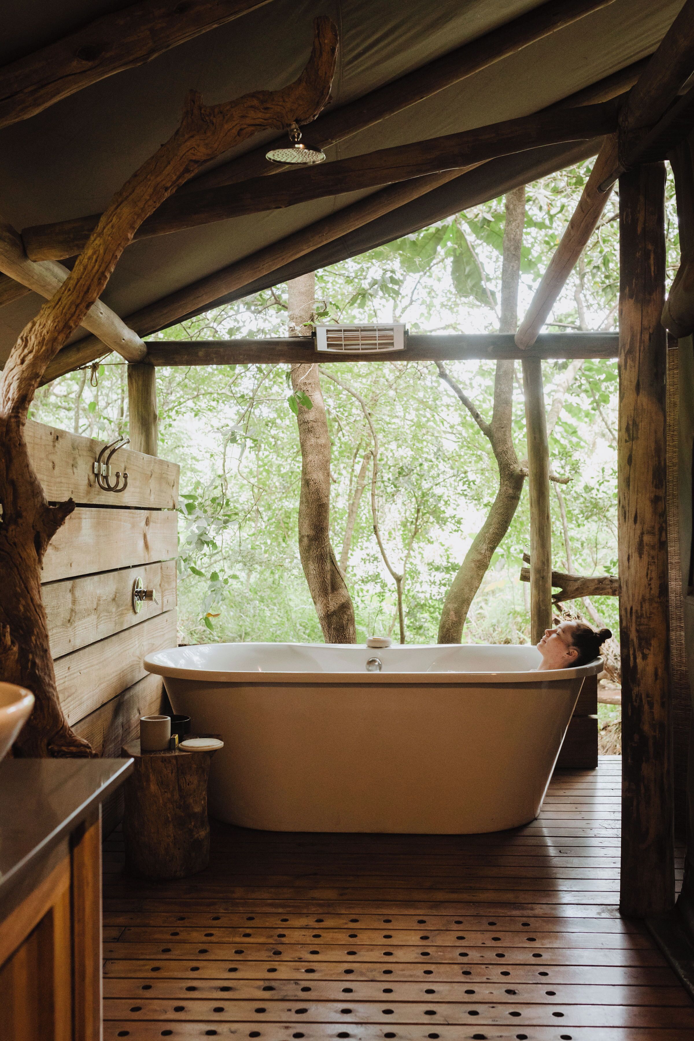 A rustic wooden cabin with a large bathtub under a tree.