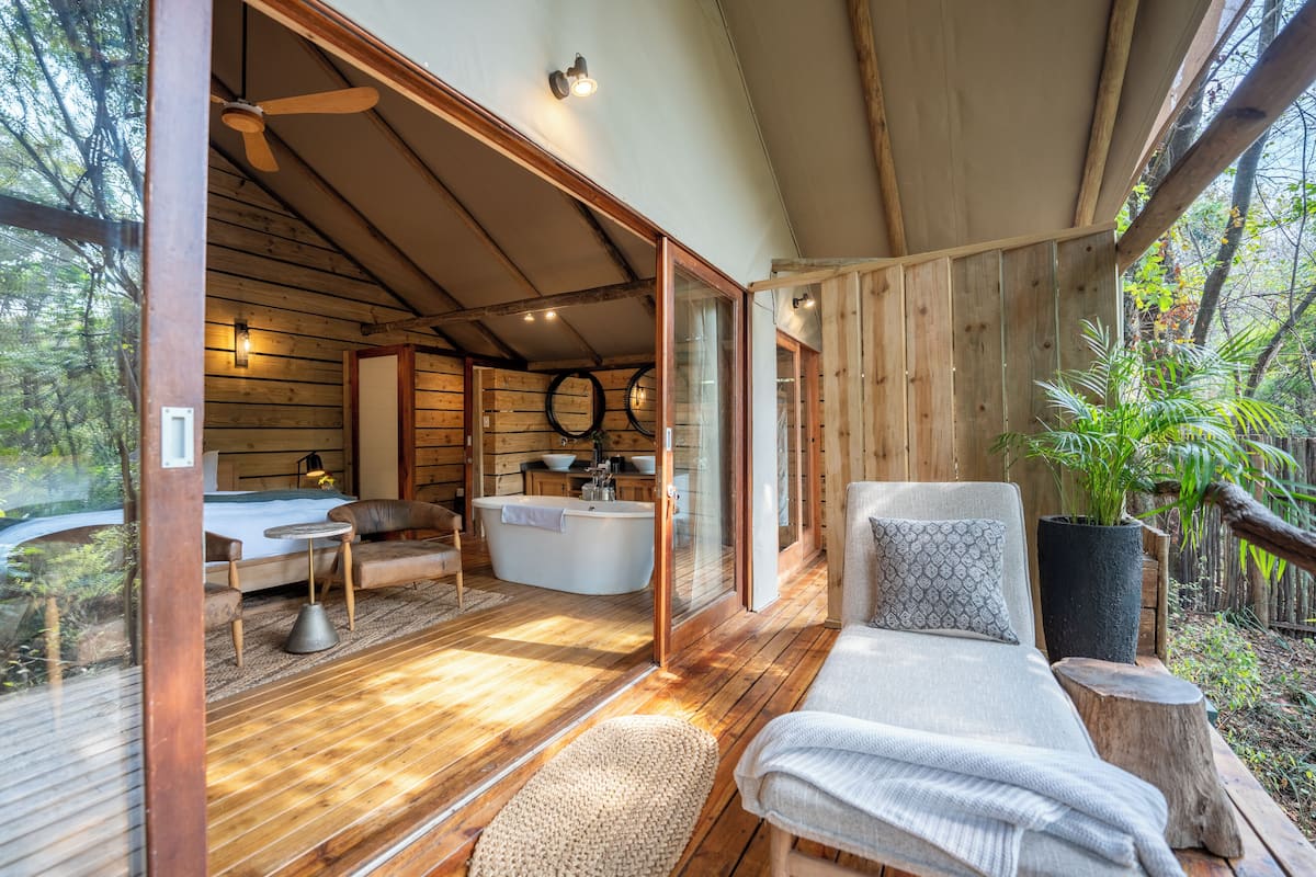 A wooden cabin with a large window, a bathtub, a sofa, and a dining table.