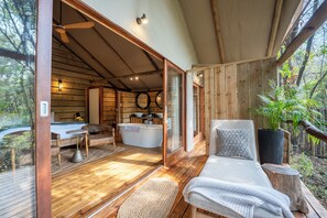 A wooden cabin with a large window, a bathtub, a sofa, and a dining table. - Summerfields Rose Retreat & Spa (Mbombela)