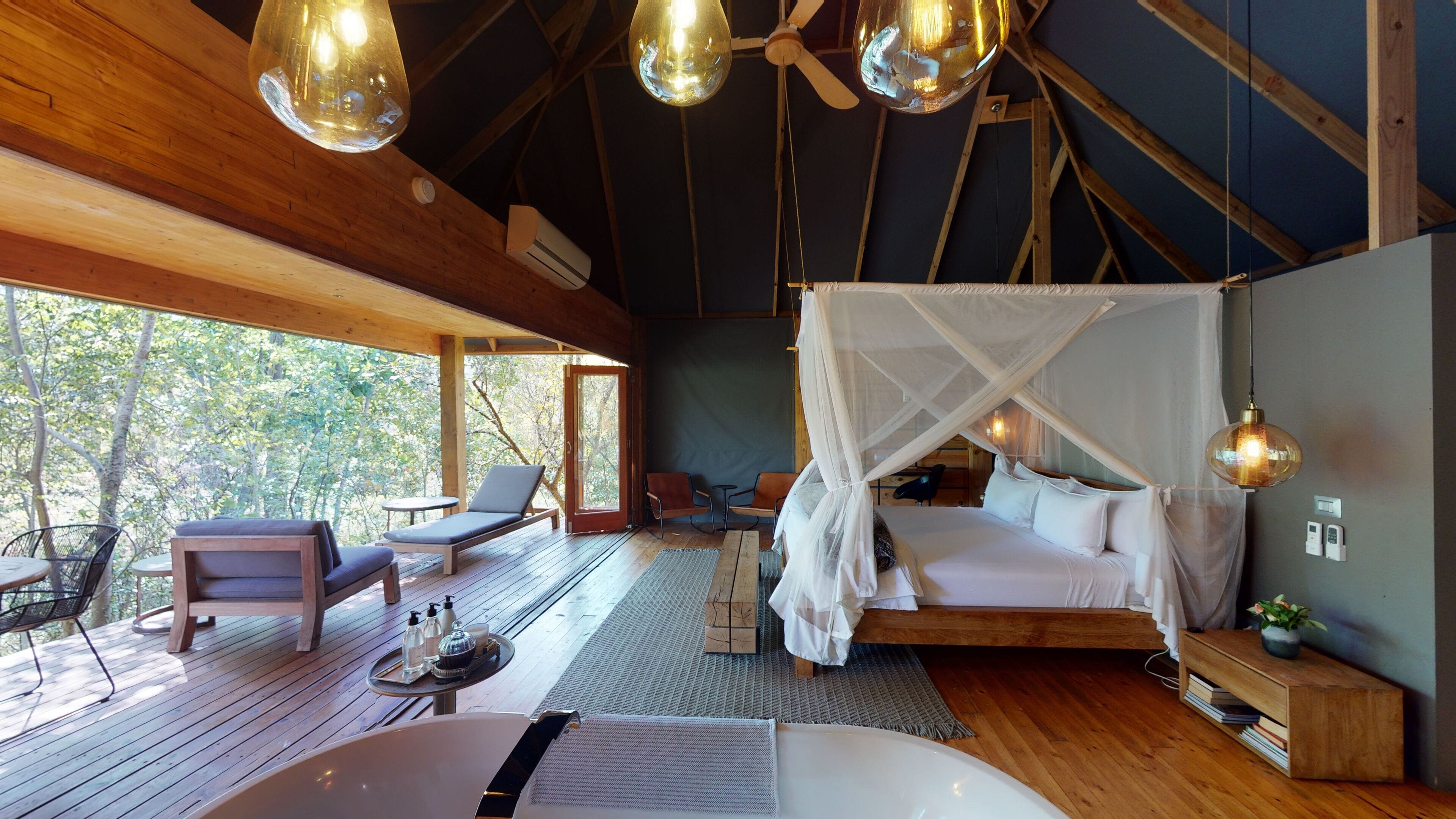 Ein gemütliches Schlafzimmer mit Baldachinbett, Holzboden und Blick auf Bäume durch große Fenster.