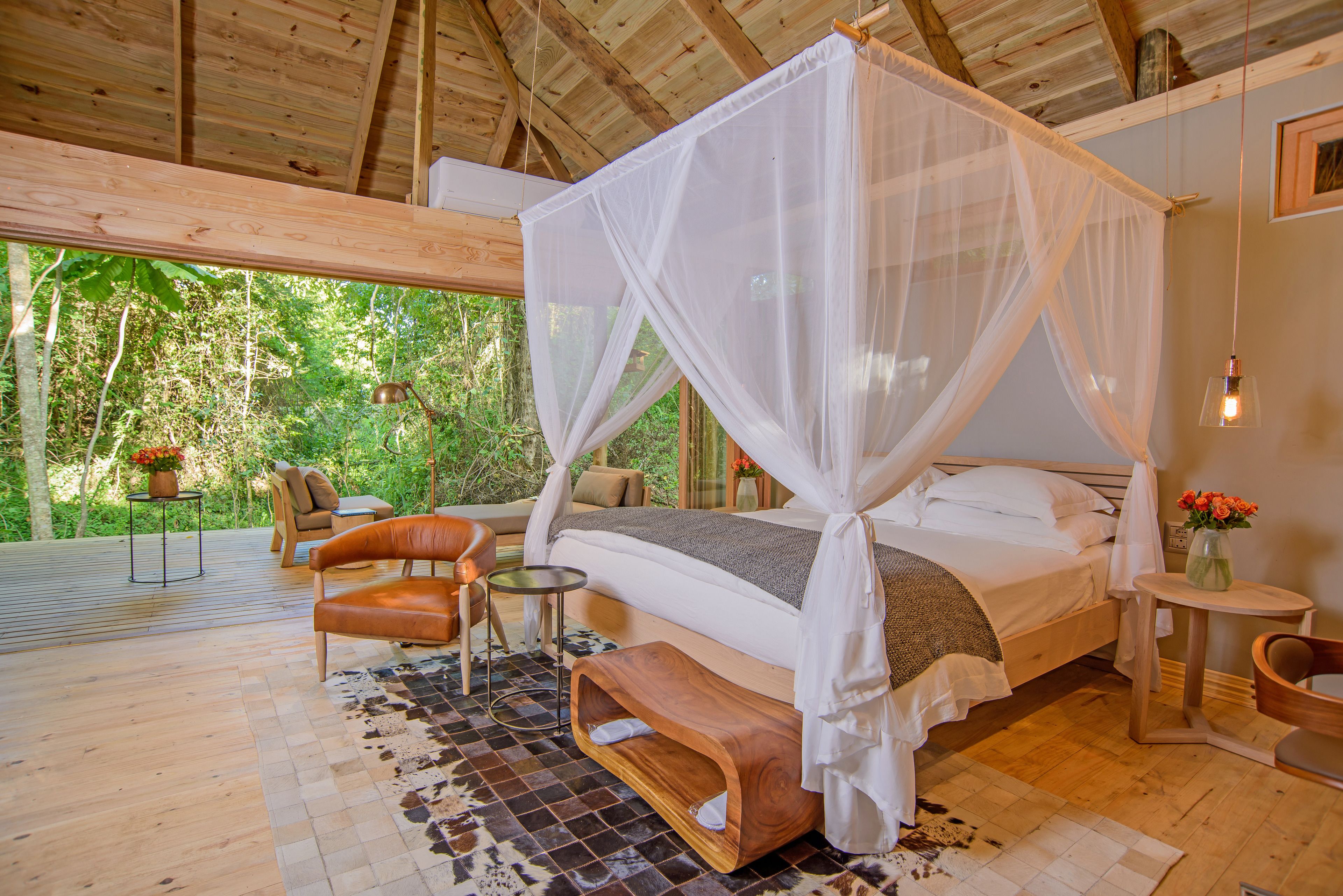 A spacious bedroom with a canopy bed, wooden flooring, and a view of the outdoors.
