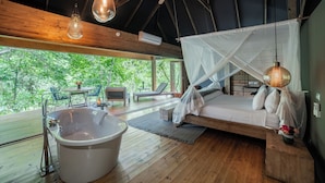 Una cabaña de madera con una bañera grande, una cama con dosel y vistas al bosque.