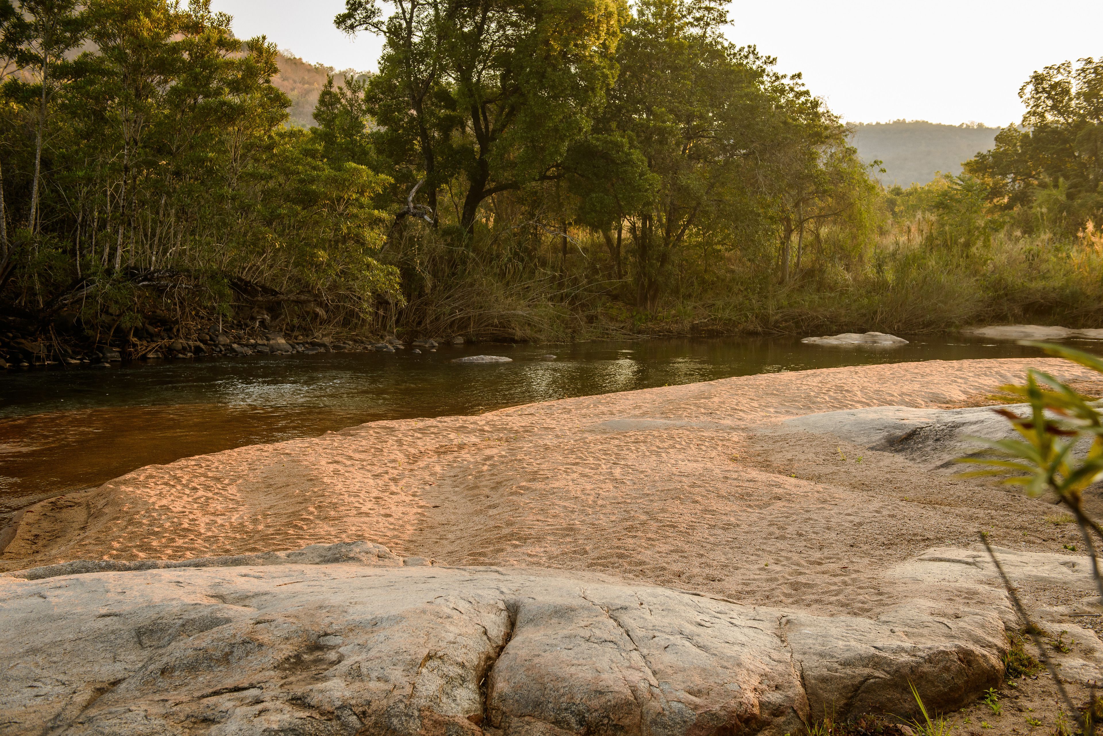 Un río con una orilla arenosa y grandes rocas en primer plano.