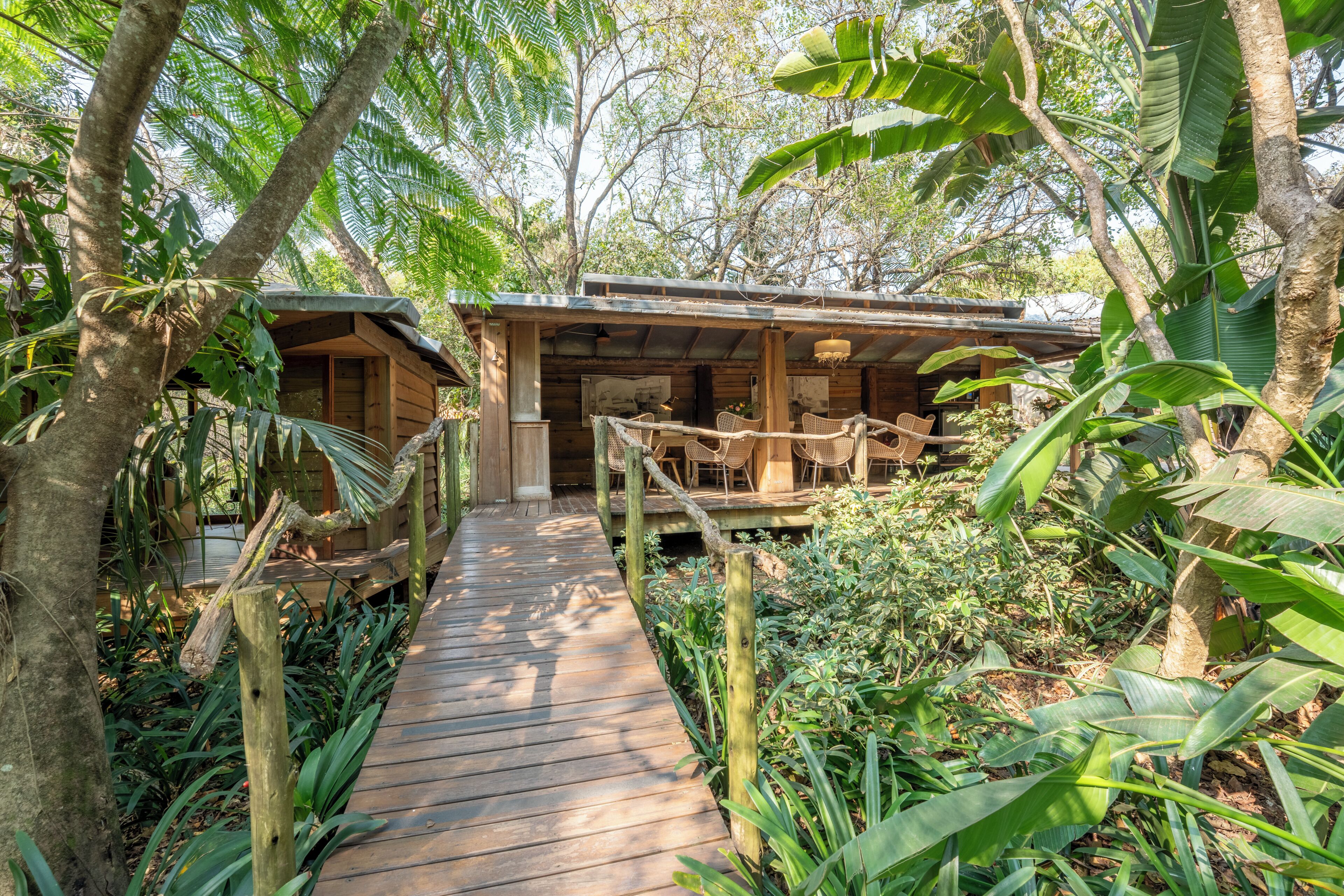 A wooden pathway leading to a rustic building surrounded by lush greenery.