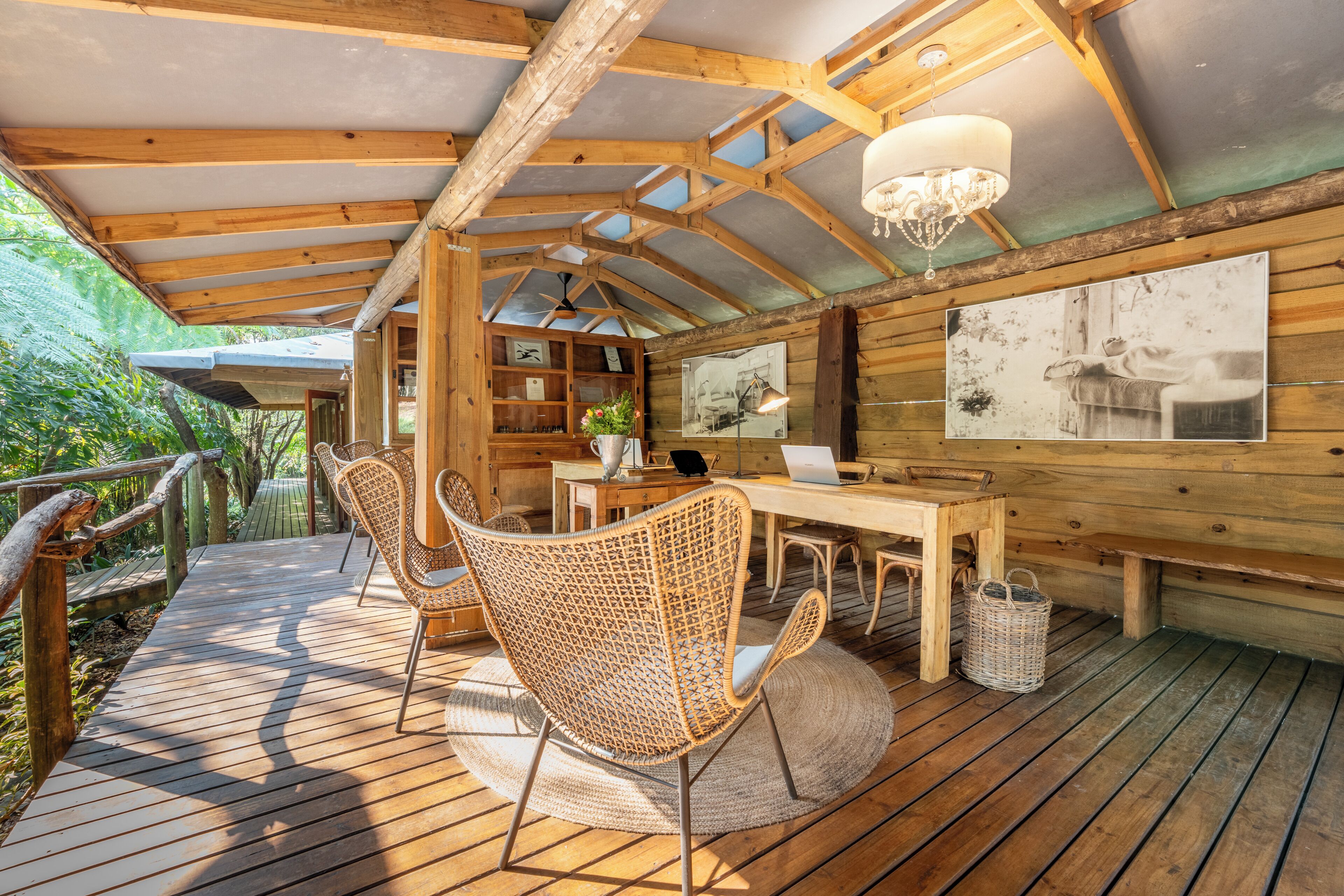 Een houten terras met wickerstoelen, een tafel en een kroonluchter.