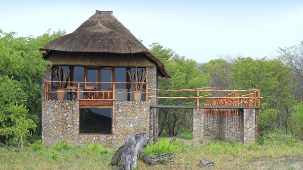 Un bâtiment rustique à toit de chaume, doté d’une base en pierre et entouré de verdure.