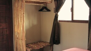 Une pièce avec un banc en bois, un lit recouvert d’une courtepointe rose, une porte en bois et une fenêtre avec des rideaux.