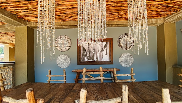 A rustic dining area with a wooden table and benches, surrounded by decorative wall art and a hanging light fixture. - Gwango Heritage Resort (Dete)