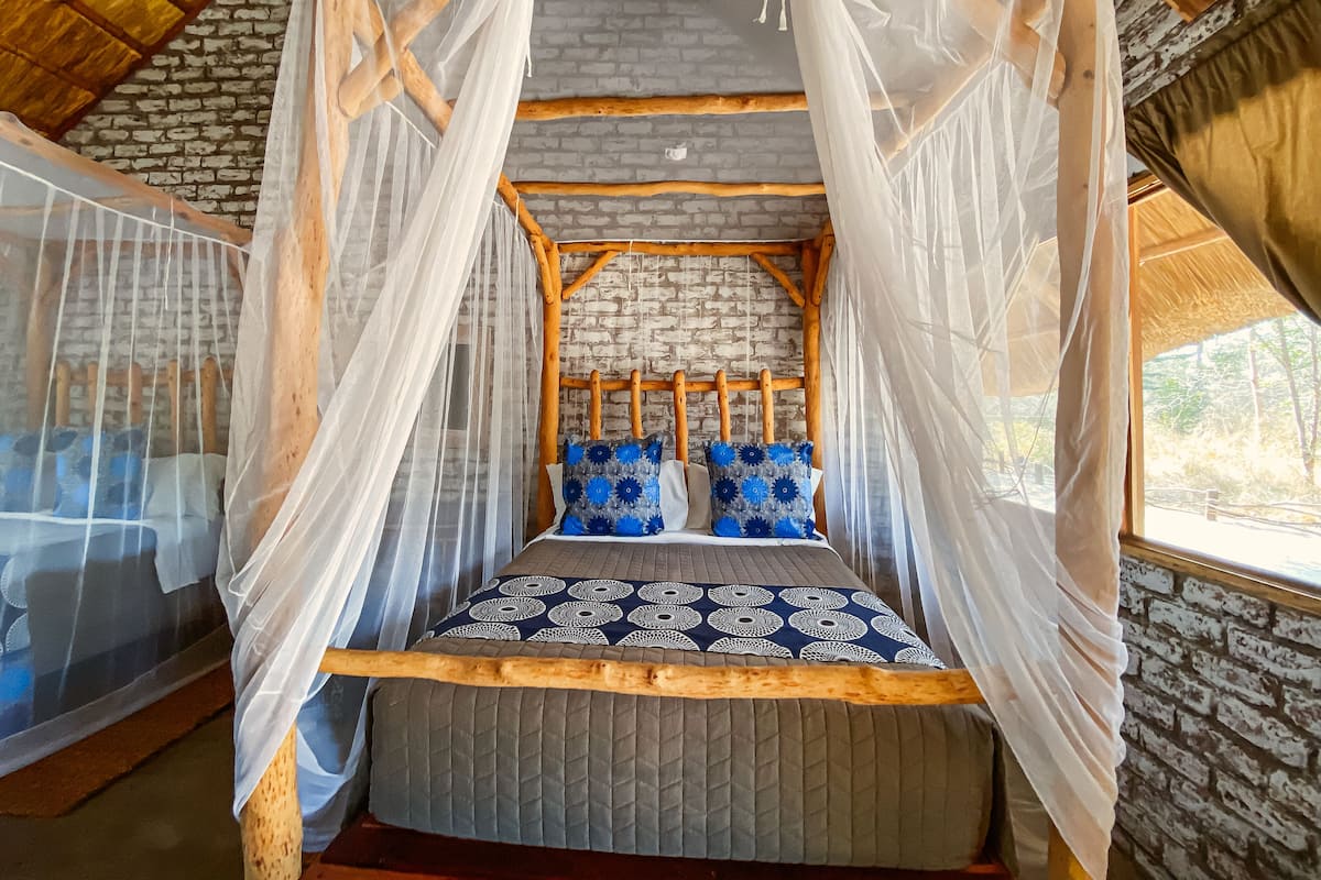 A bed with a canopy, a brick wall, and a wooden ceiling.