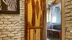 A rustic wooden door with a unique grain pattern, leading to a room with a stone wall and a bed with a canopy. - Gwango Heritage Resort (Dete)