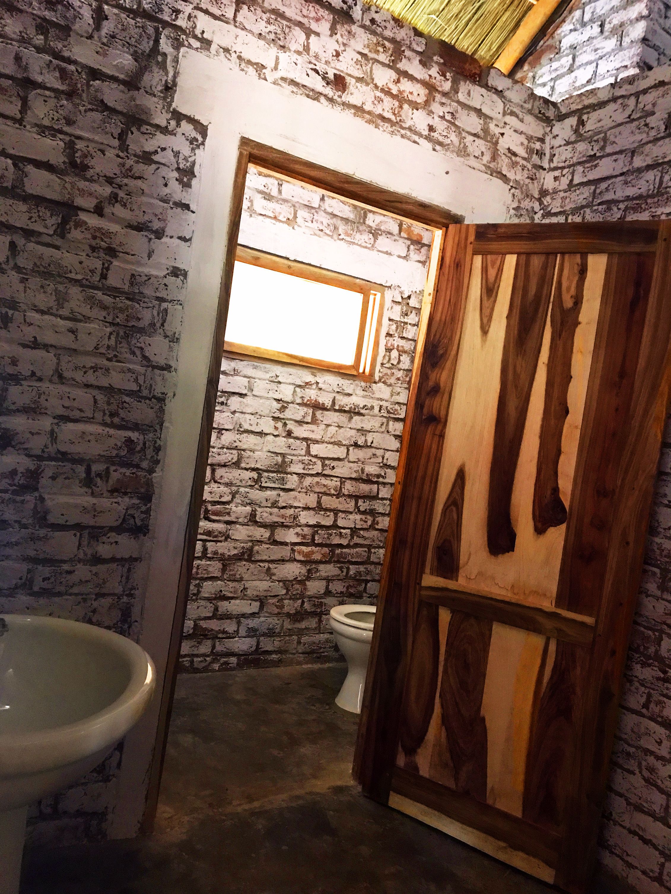 A bathroom with a rustic brick wall, a wooden door, and a window.