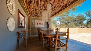 A dining area with a long wooden table and chairs, surrounded by walls adorned with various artworks, under a thatched roof. - Gwango Heritage Resort (Dete)