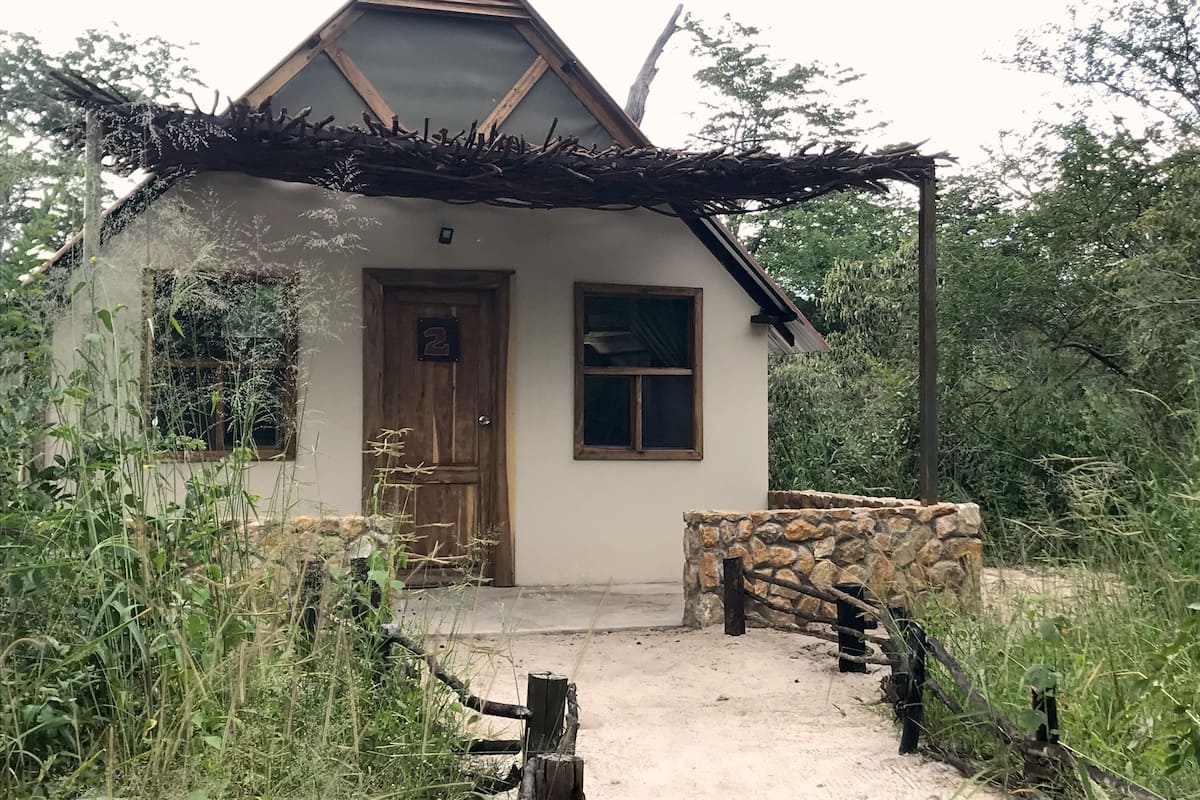 A small, rustic house with a stone wall entrance, a wooden door, and a window.