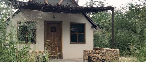 A small, rustic house with a stone wall entrance, a wooden door, and a window.