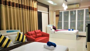 A hotel room with a bed, a red armchair, a bedside table, and a window with curtains. - Head Rock Home (Hua Hin)