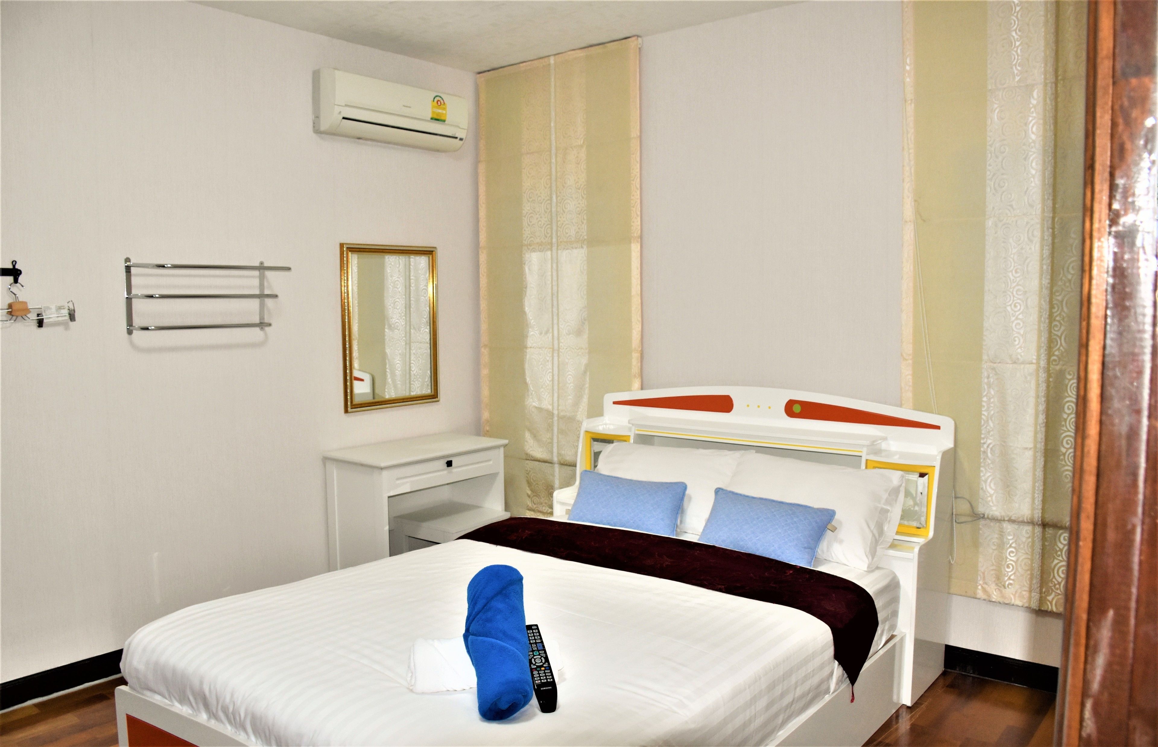 Een hotelkamer met een bed, nachtkastje, spiegel, airconditioning en een raam met gordijnen.