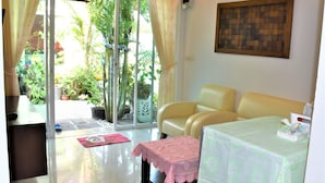 A room with a glass door leading to a garden, a sofa, a table with a tablecloth, and a wall-mounted artwork. - Head Rock Home (Hua Hin)